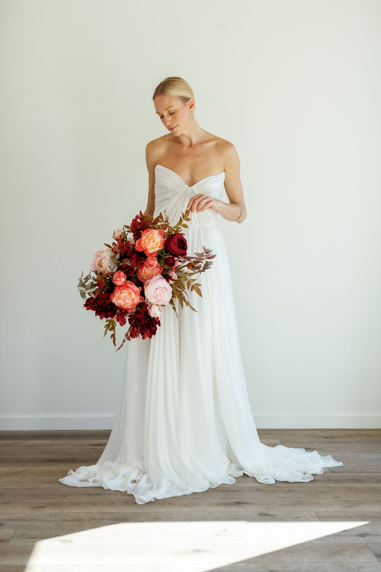 Bride in a white strapless gown holding a bouquet of flowers against a plain background