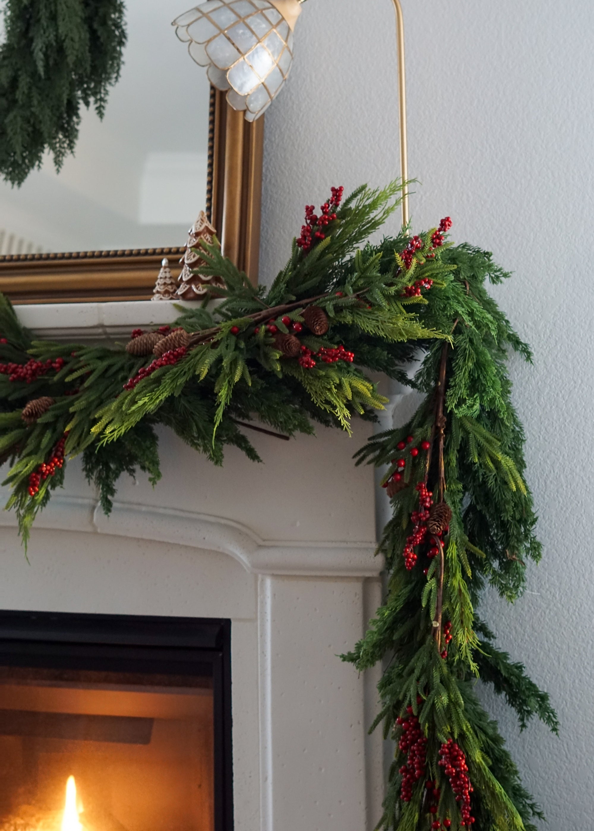 Green Christmas garland with red berries on a fireplace mantel.