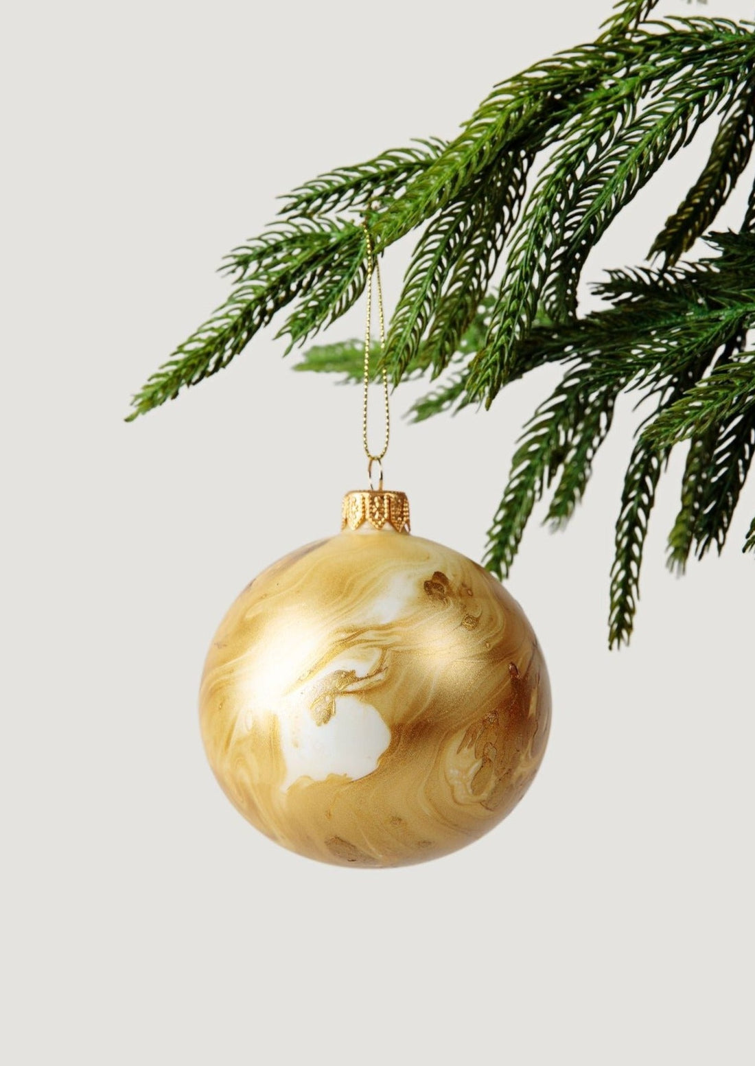 Mouth-Blown Glass Bulb Ornament in Gold Marble Hanging on Faux Pine Tree Branch