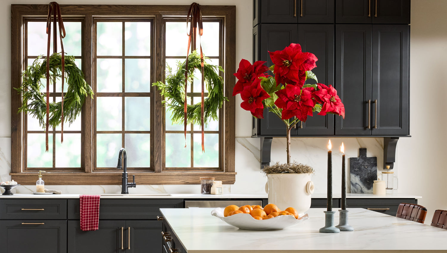 Luxe faux poinsetia plant on kitchen counter with afloral norfolk pine wreaths on windows