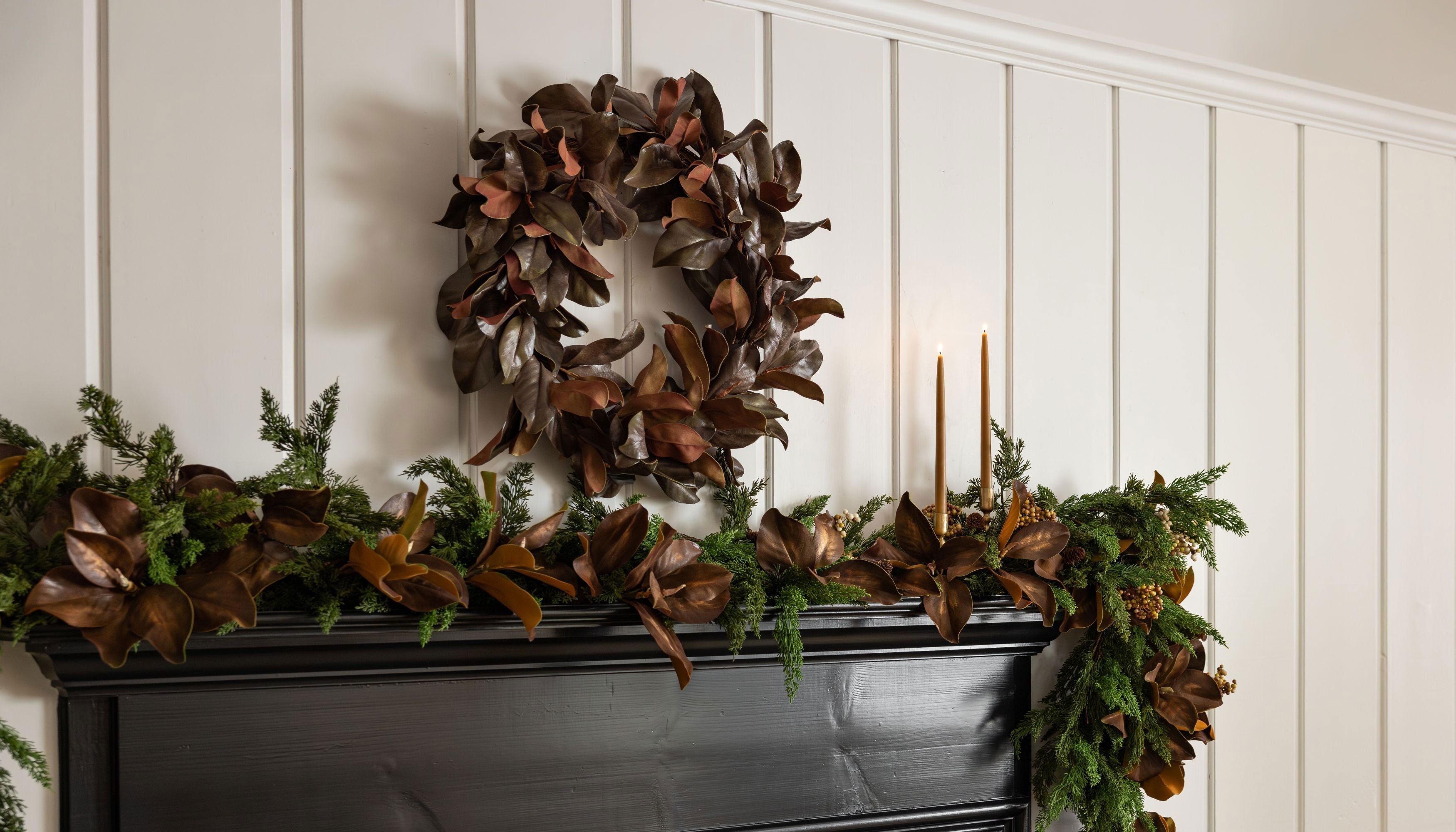 a holiday mantel with a magnolia wreath and cedar and magnolia leaf garland