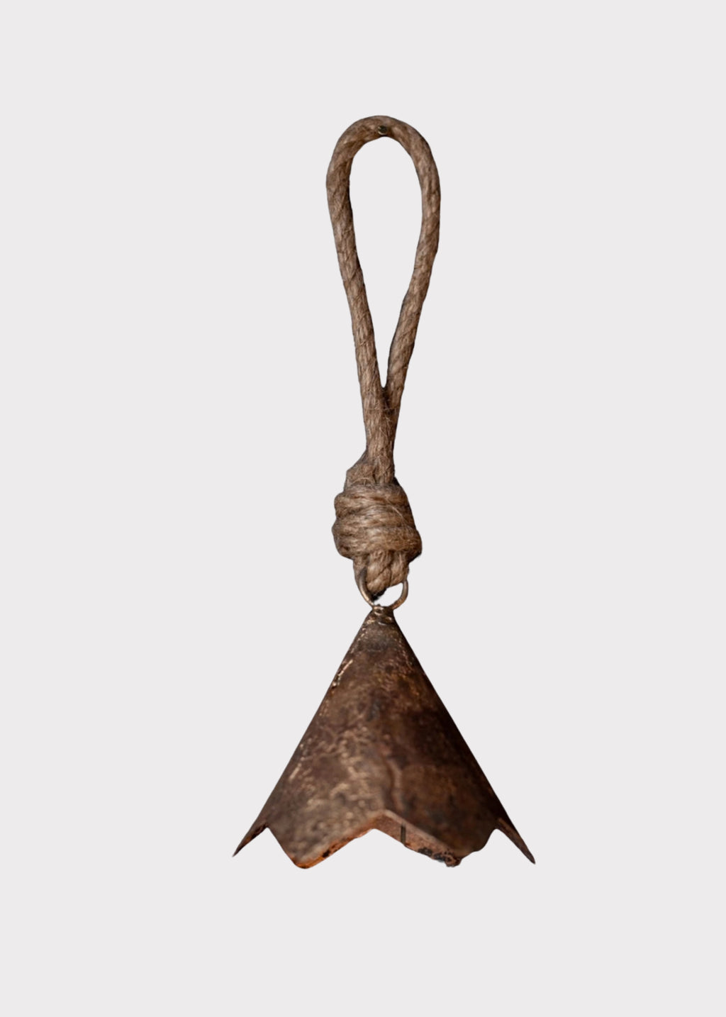 A rustic metal bell with a textured, weathered bronze-brown finish, suspended from a thick, twisted brown rope loop against a solid light gray background.