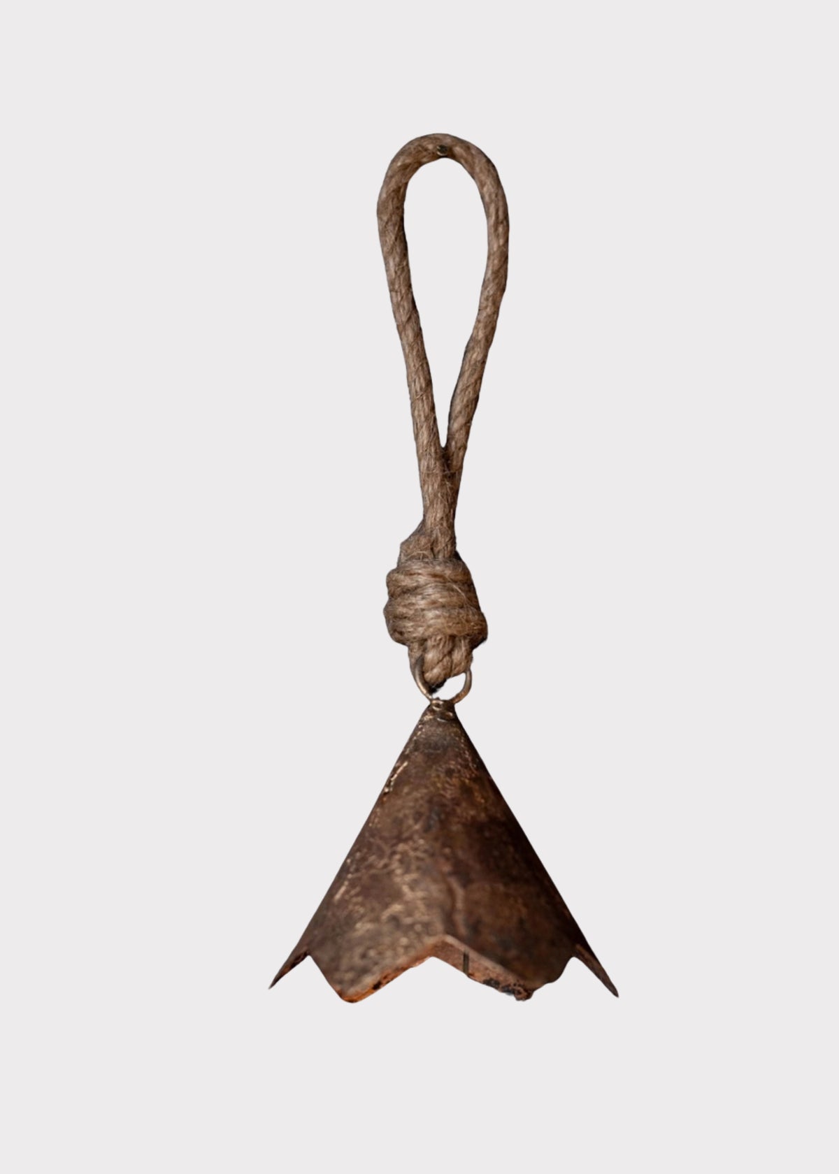 A rustic metal bell with a textured, weathered bronze-brown finish, suspended from a thick, twisted brown rope loop against a solid light gray background.