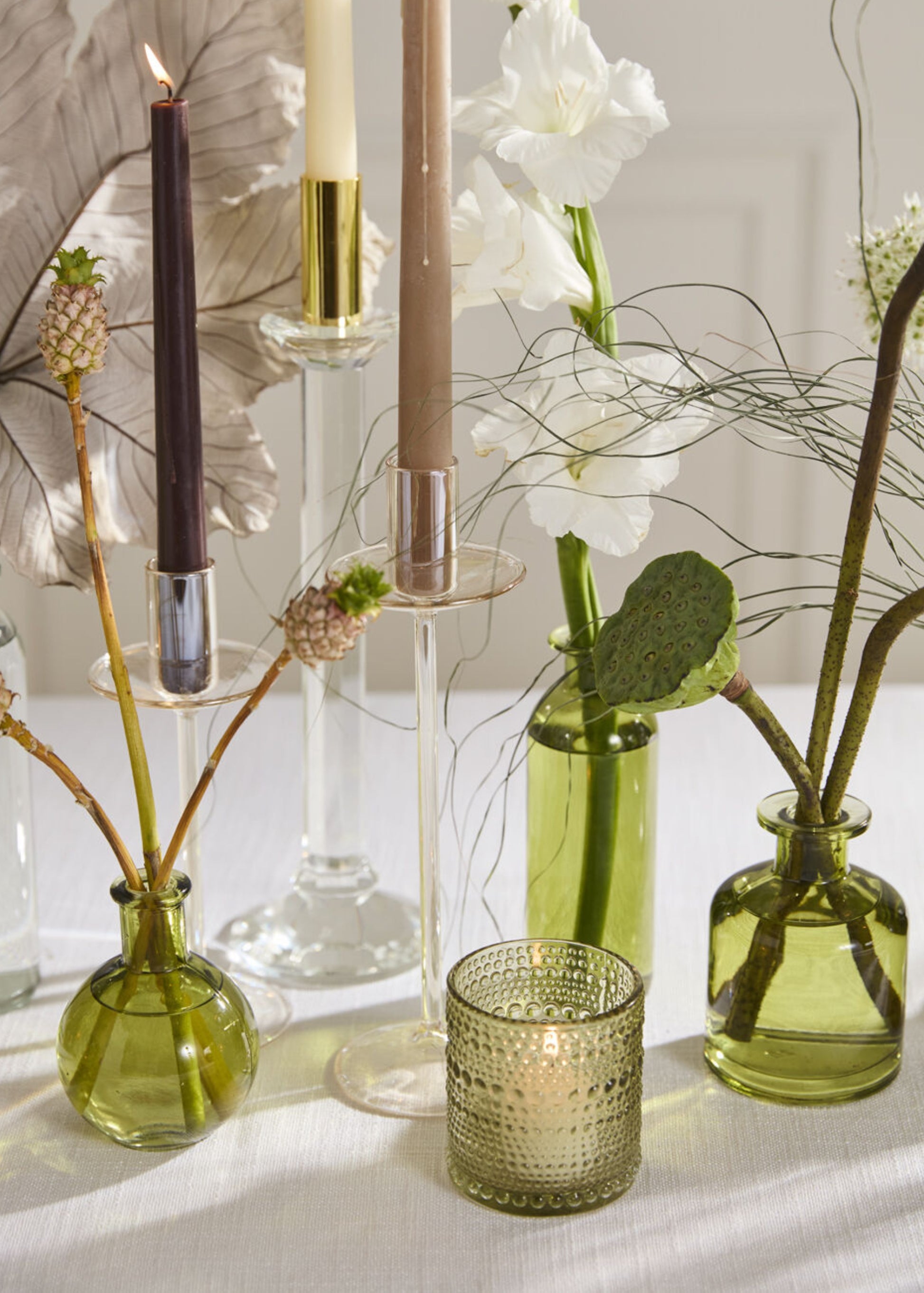 Decorative setup with candles, green vases, and flowers 