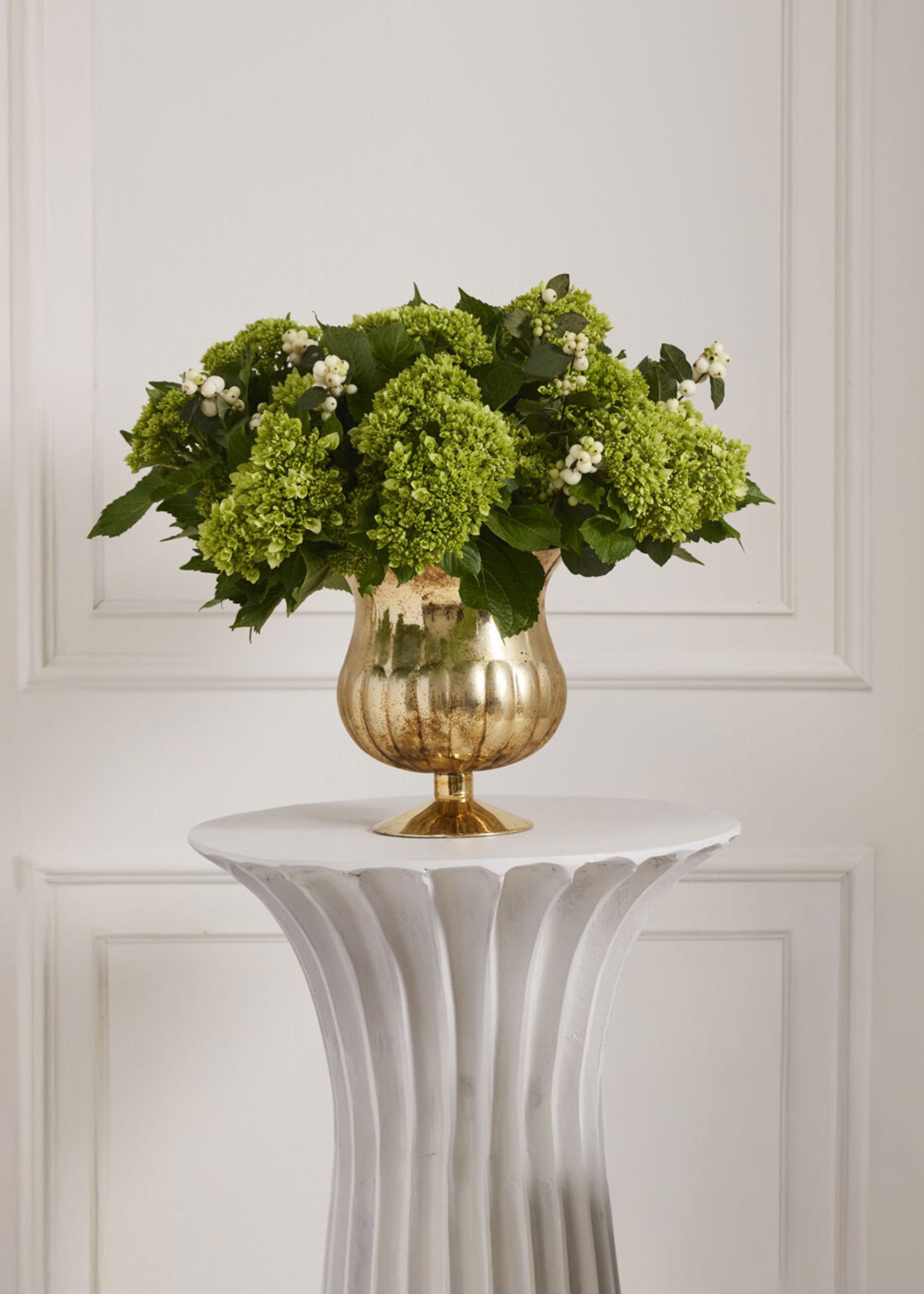 Gold vase with green flowers on a white pedestal 
