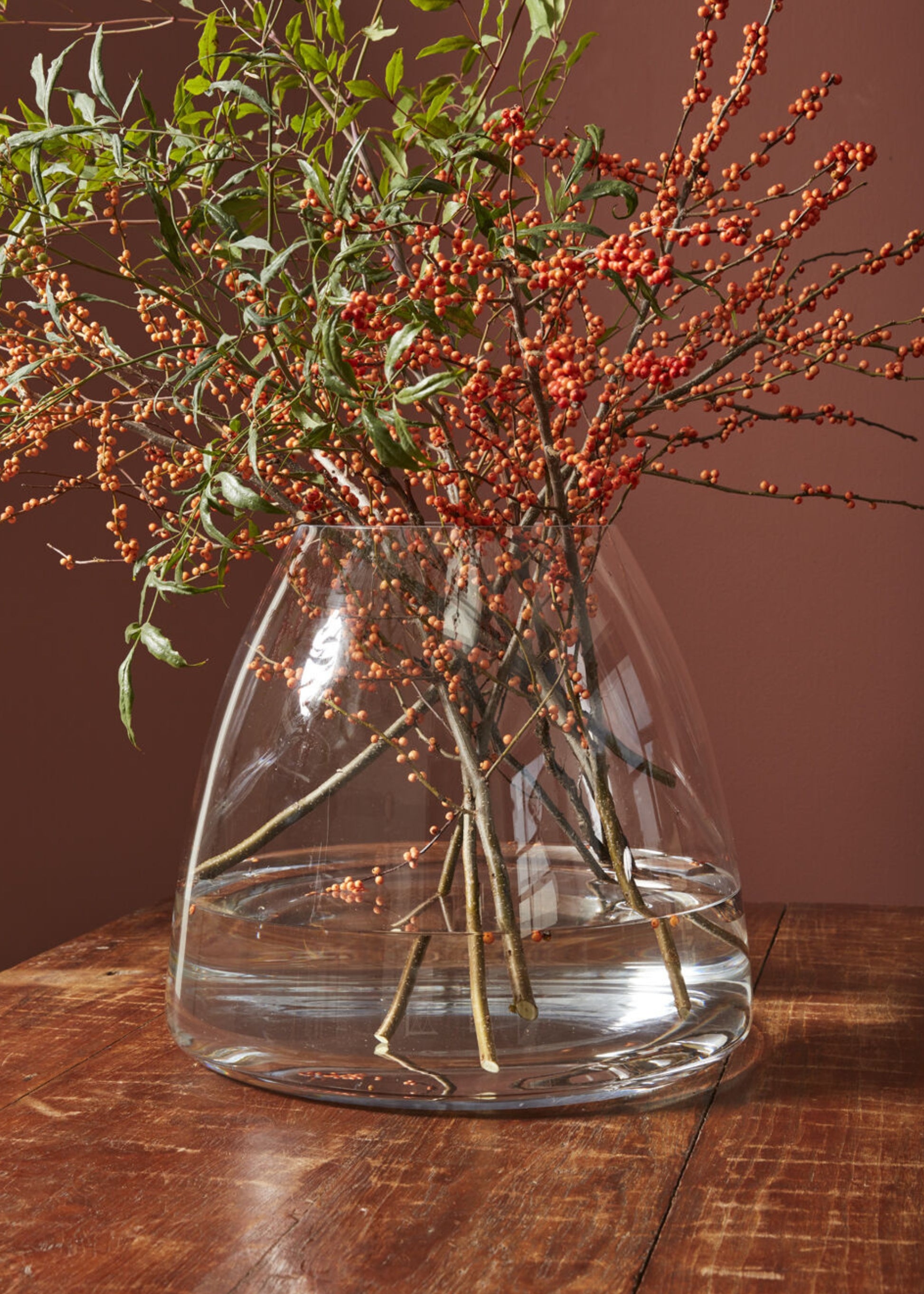 Clear glass vase with branches and berries on a wooden surface