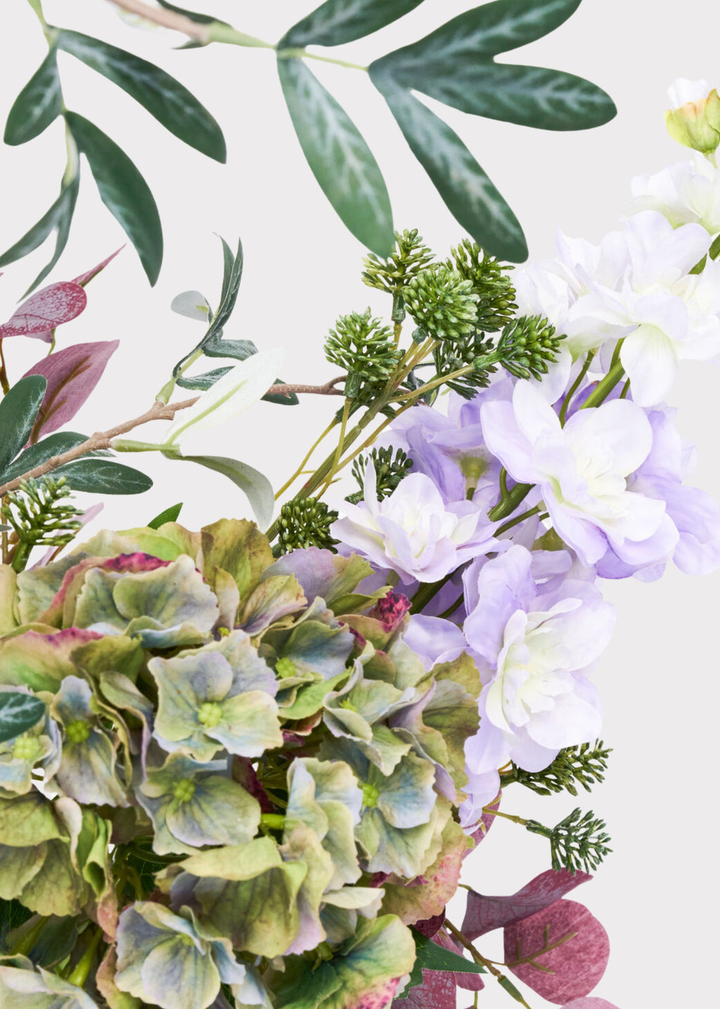 An assortment of artificial floral stems and greenery, featuring green hydrangeas, light purple flowers, dusty burgundy leaves, and textured green foliage