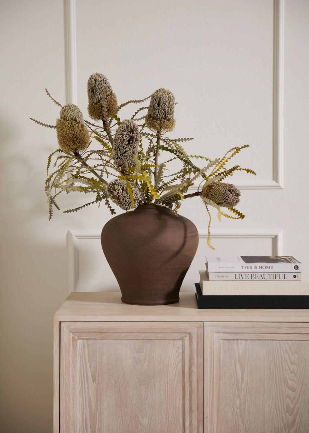 brown stoneware vase with proteas on a cabinet