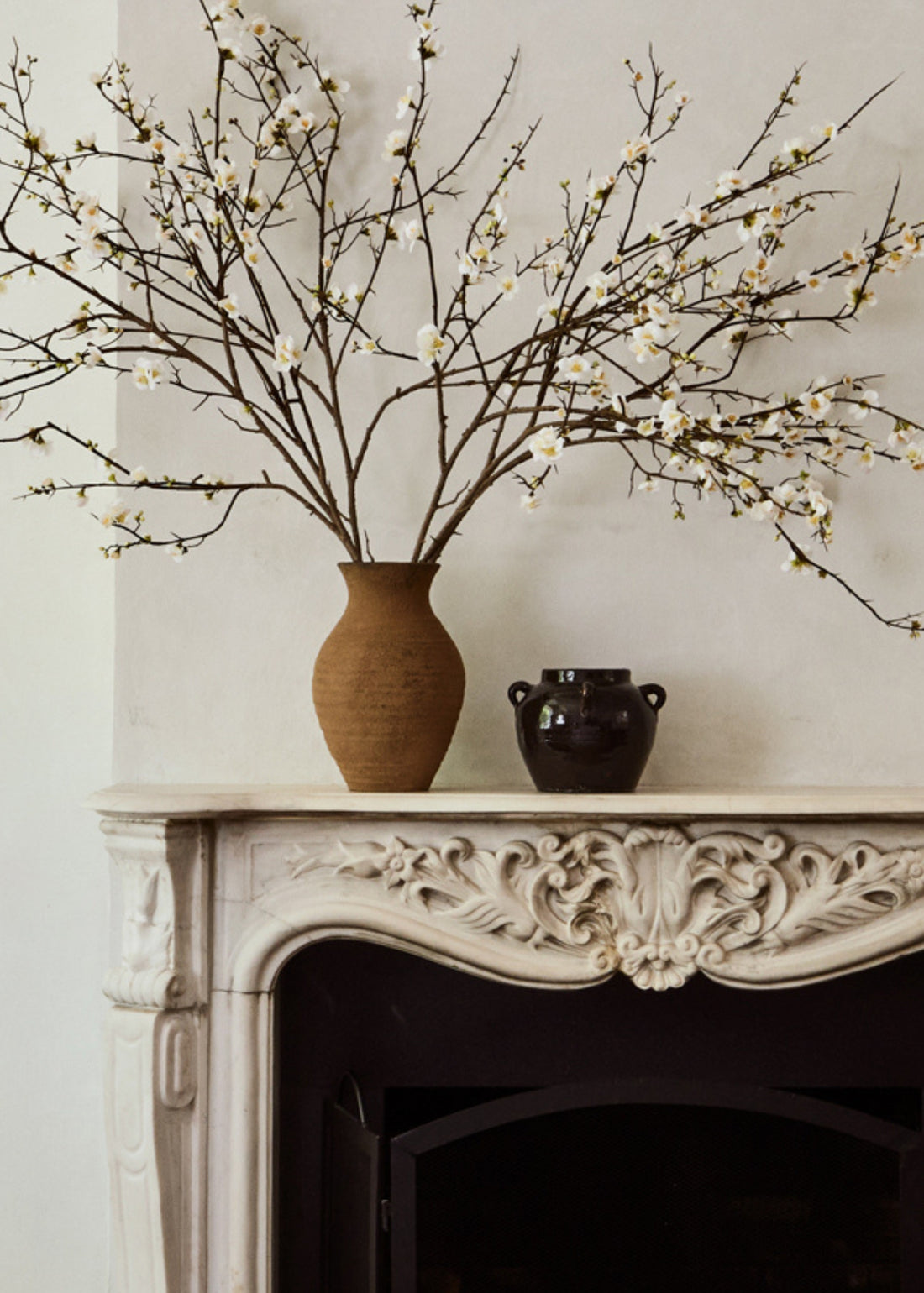 Decorative mantel with a vase of quince branches and black pot