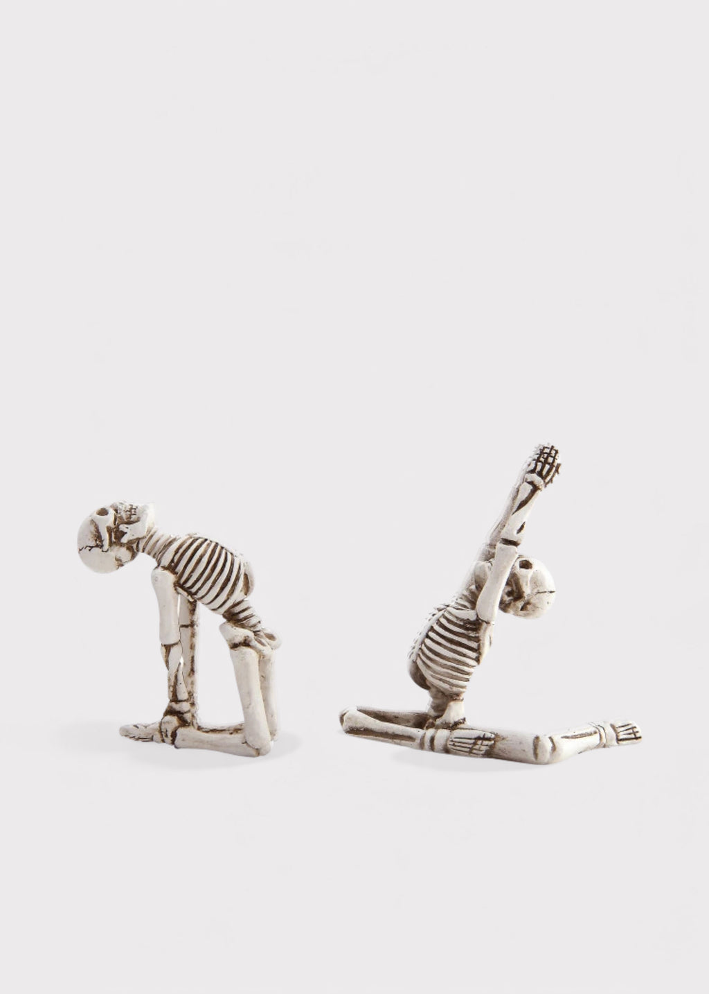 Two small skeleton figurines posed dynamically on a light gray background, one bending forward and the other stretching upward.