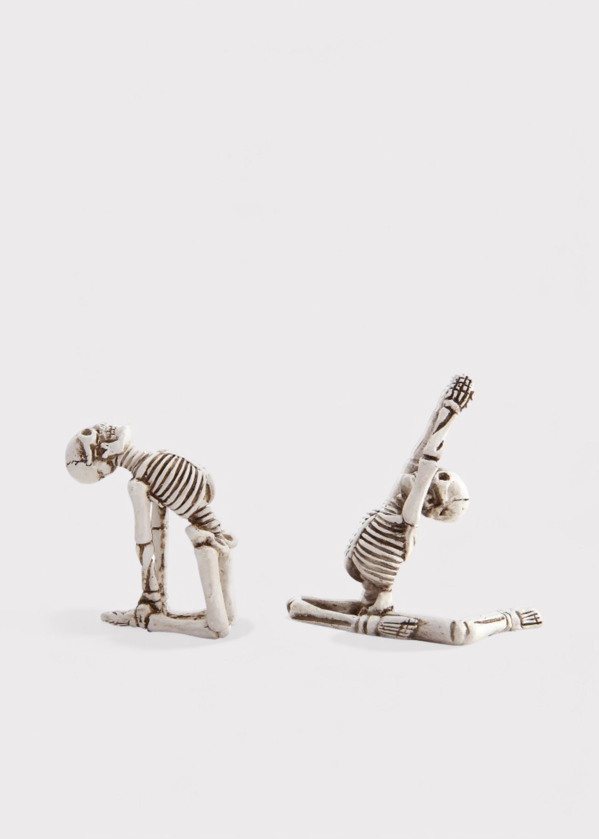 Two small skeleton figurines posed dynamically on a light gray background, one bending forward and the other stretching upward.