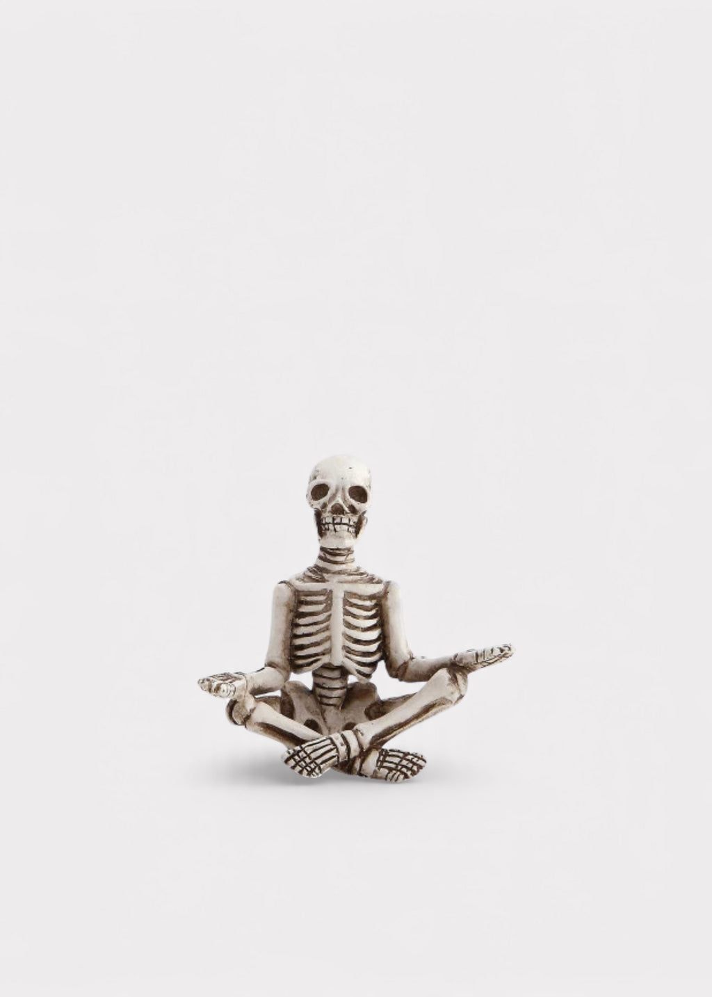 A small decorative skeleton figurine seated in a lotus position with one hand raised, shown against a plain light gray background.