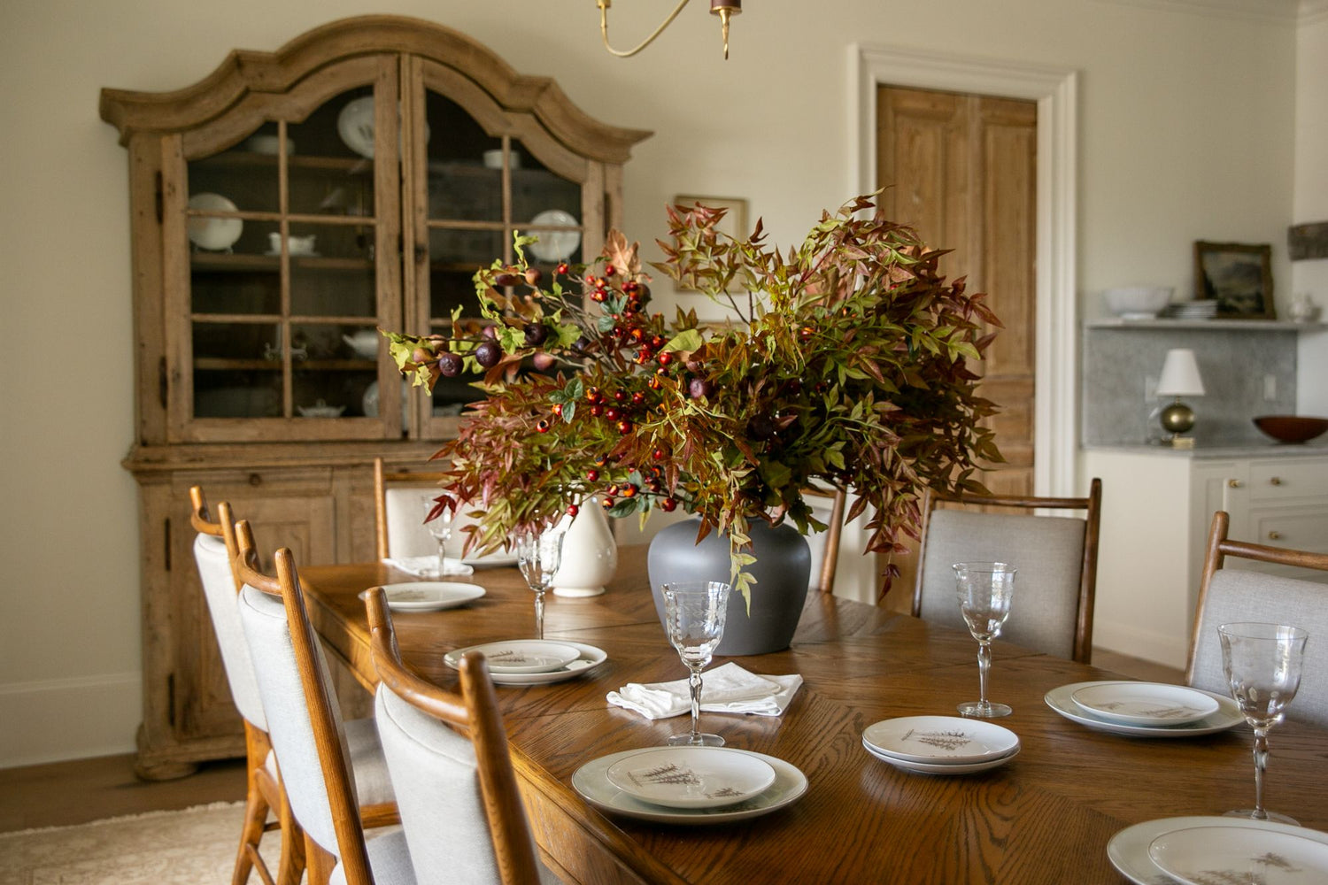 Dining room with a wooden table set for dinner, featuring a large floral arrangement.