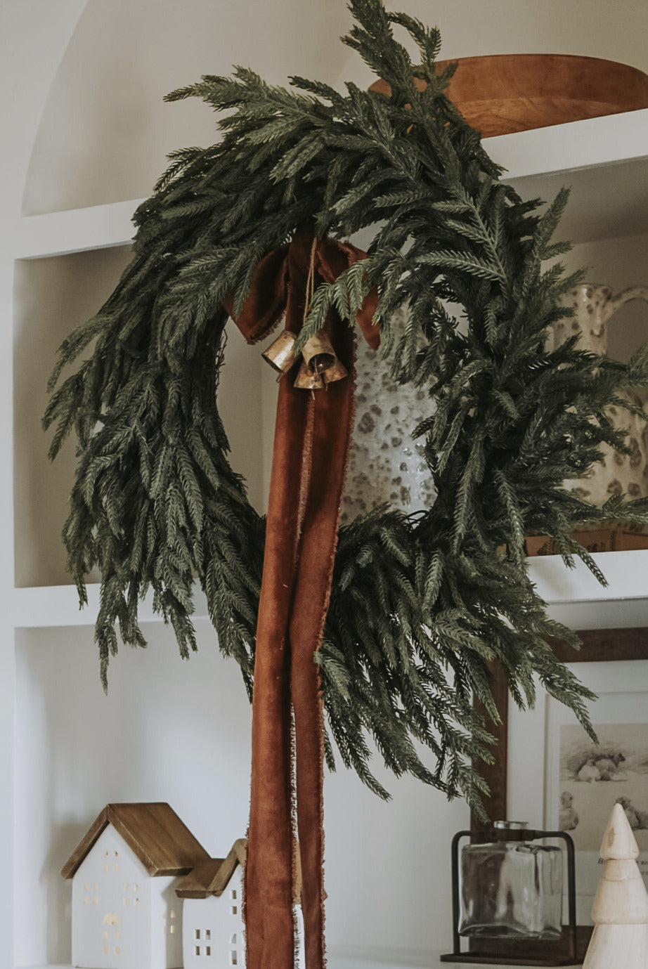 Decorative wreath with ribbons and bells hanging on a white shelf.