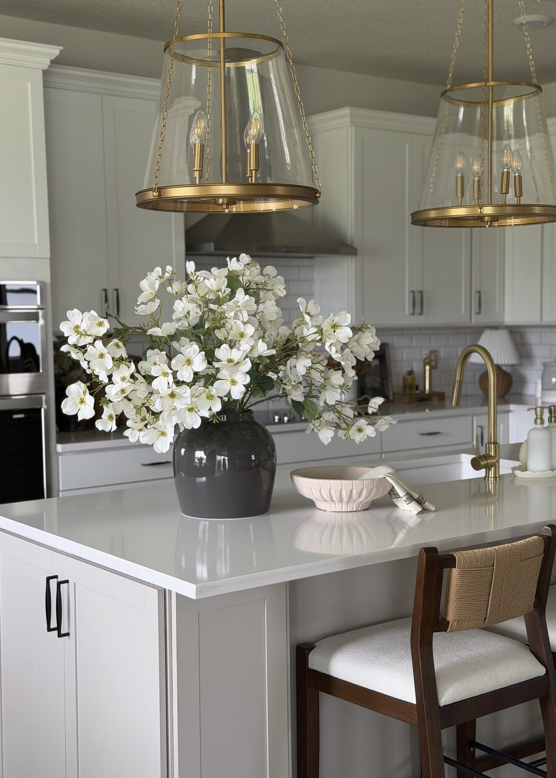 Modern kitchen with white cabinets, gold pendant lights, and a vase of white flowers on the island.
