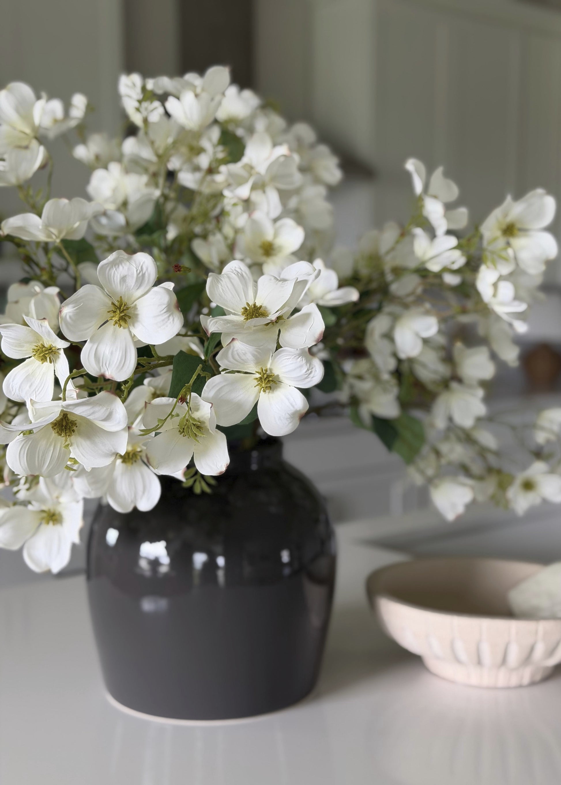Black vase with white flowers on a light surface