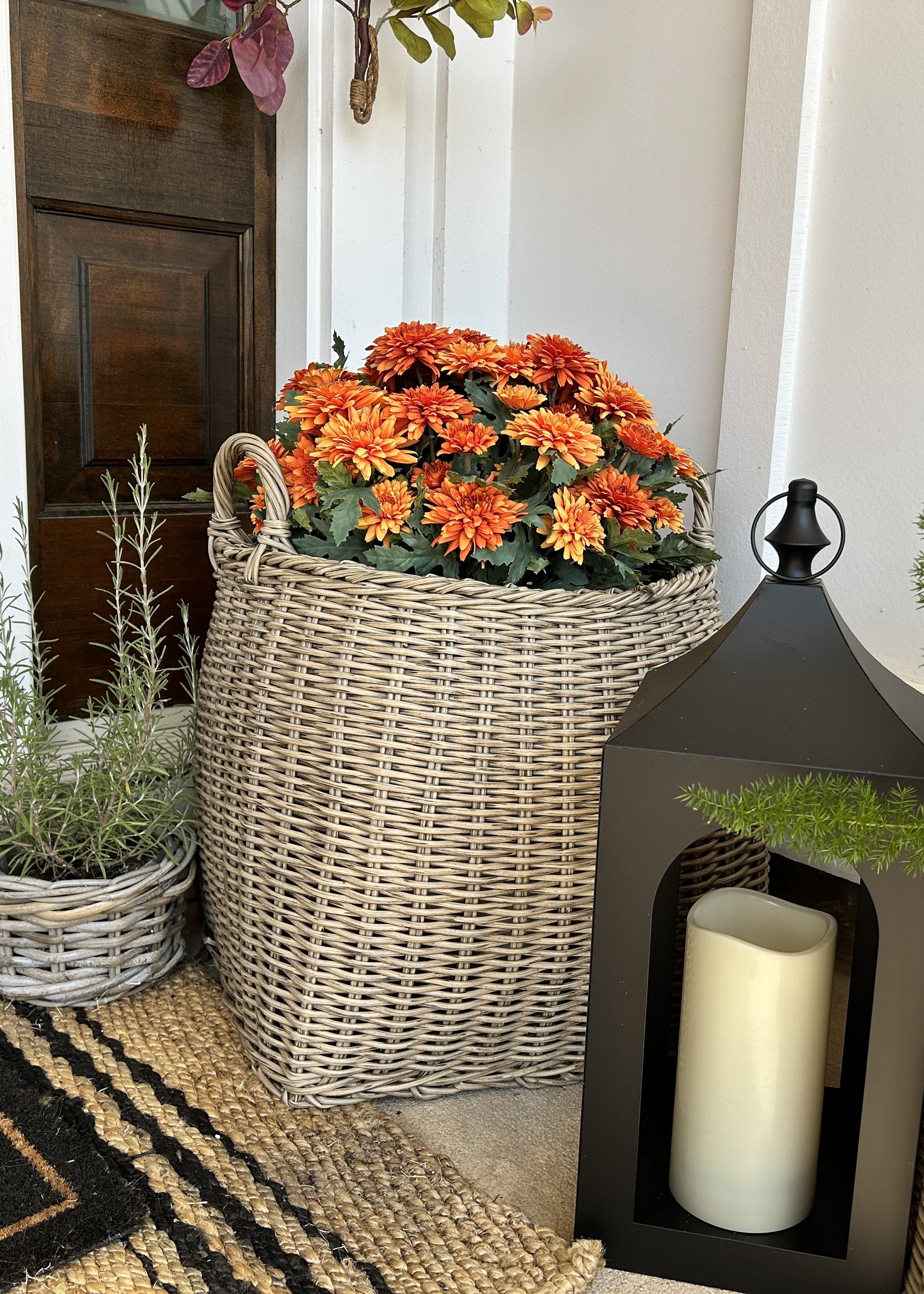 Wicker basket with orange flowers on a porch with a lantern and plants.