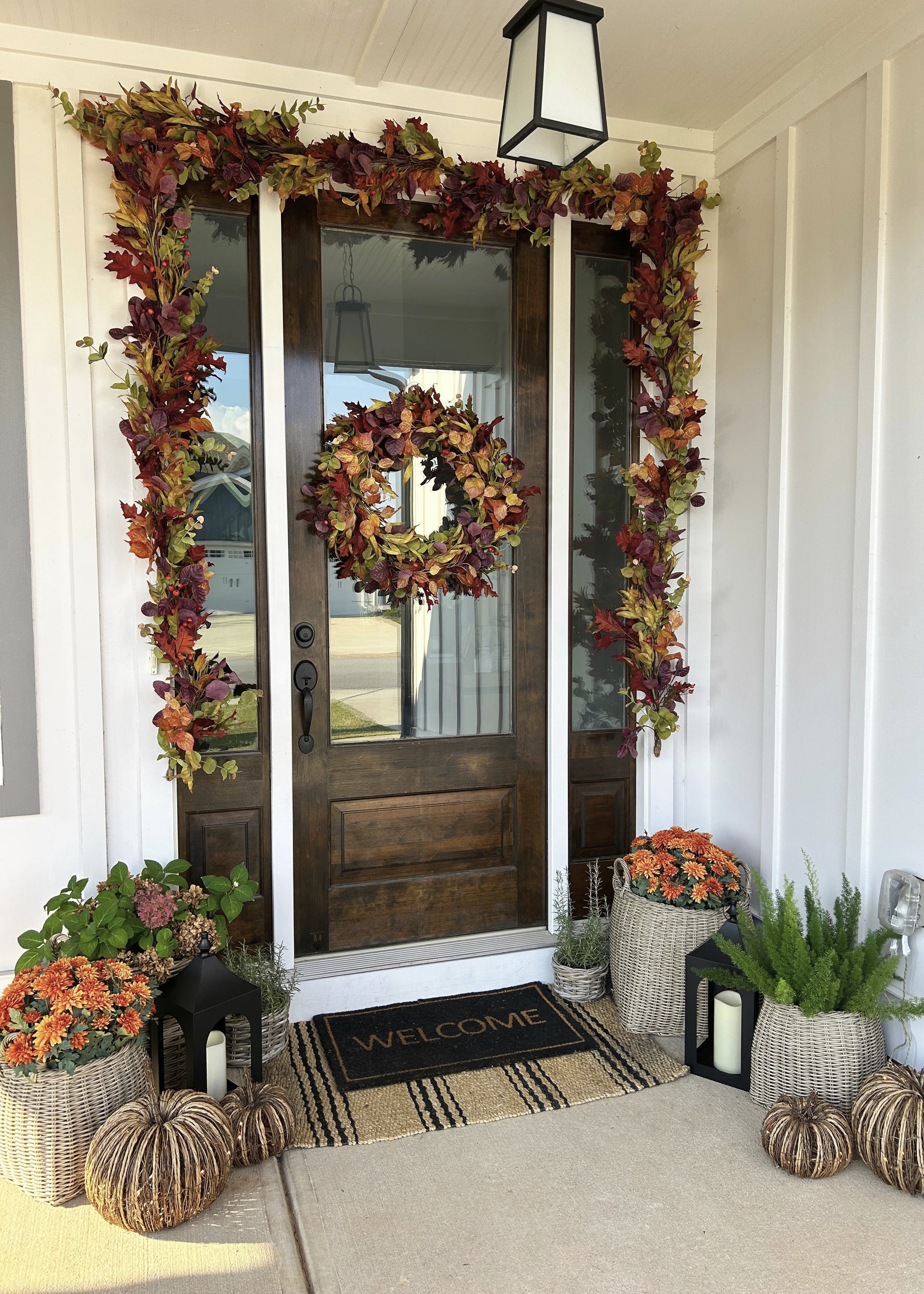 Decorative autumn wreath and garlands on a door with pumpkins and a welcome mat.