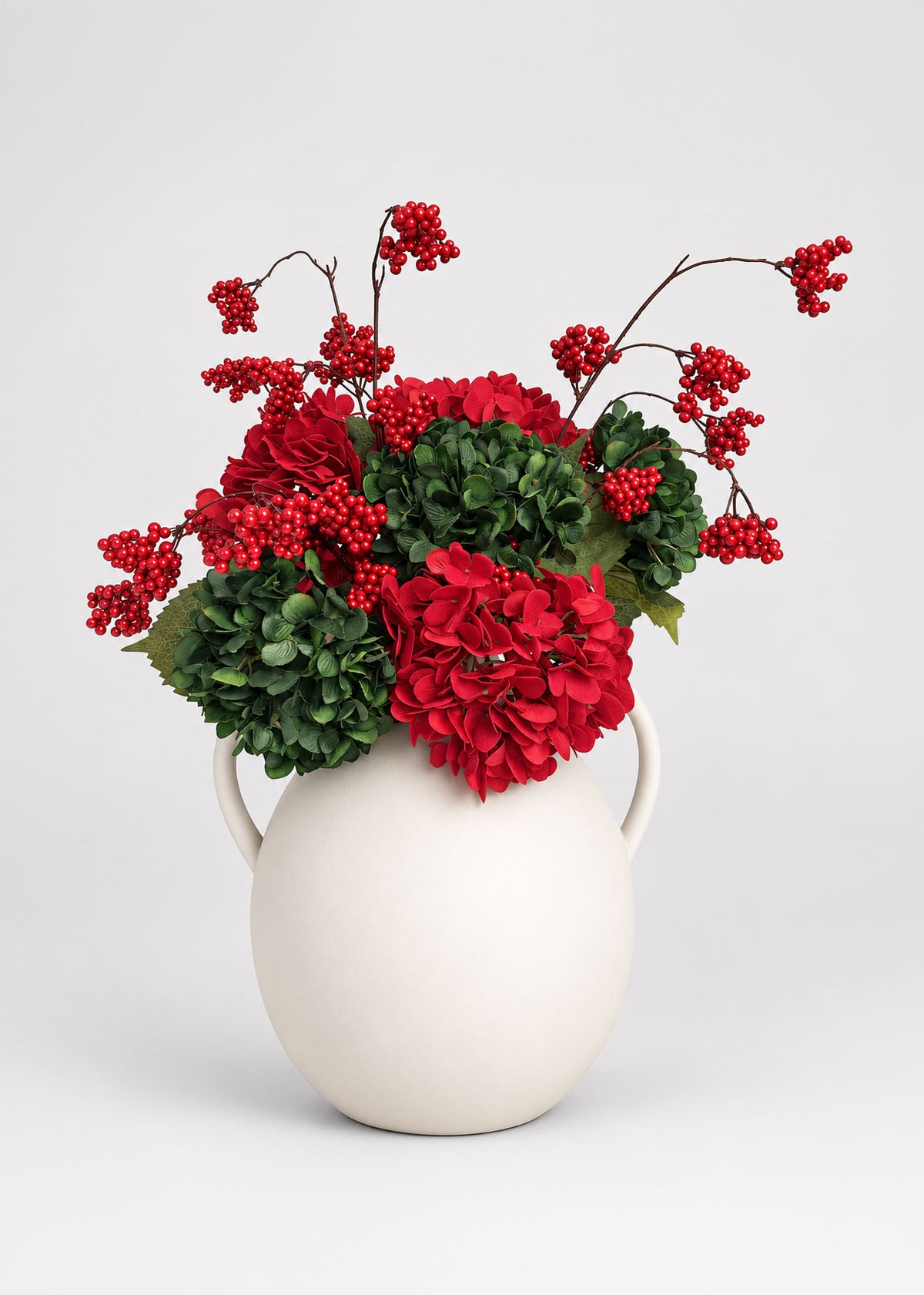 red and green hydrangea arrangement with red berries in the afloral white jug vase
