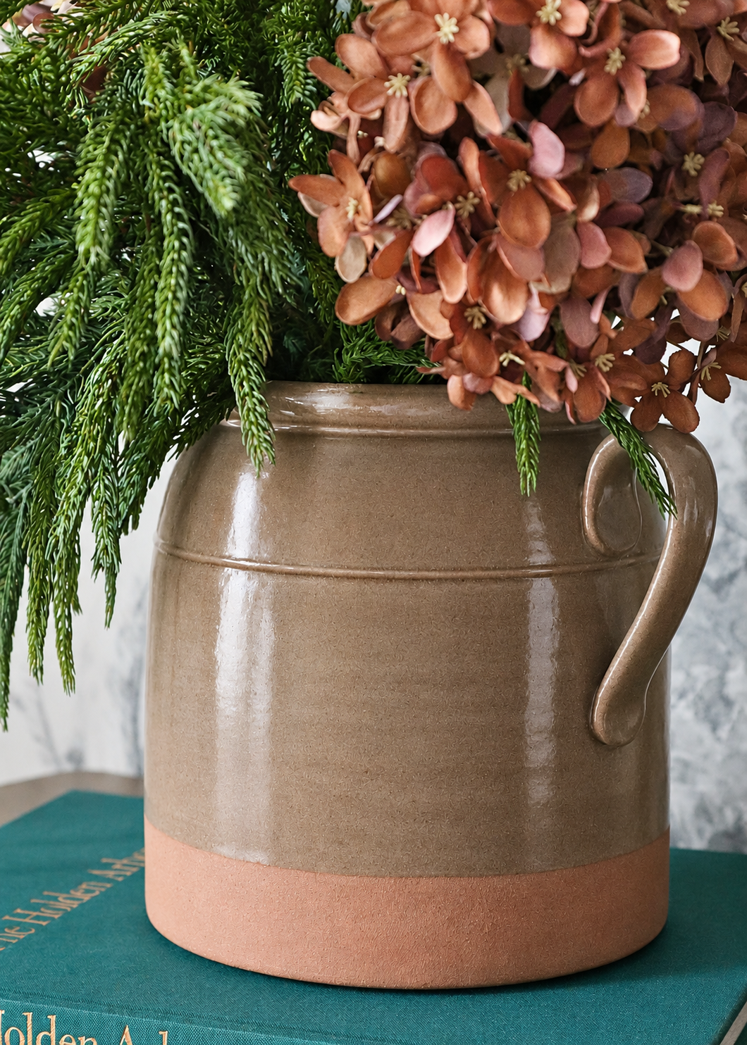 Close-up of a crock styled with brown hydrangeas and norfolk pine