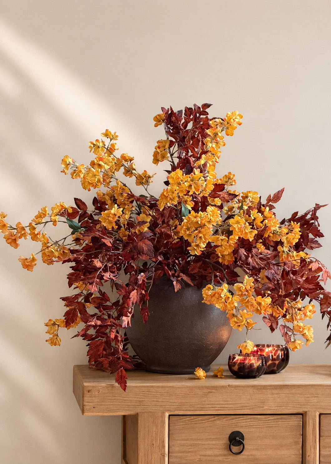 yellow cherry blossoms paired with orange brown cimicifuga leaves in a stoneware vase