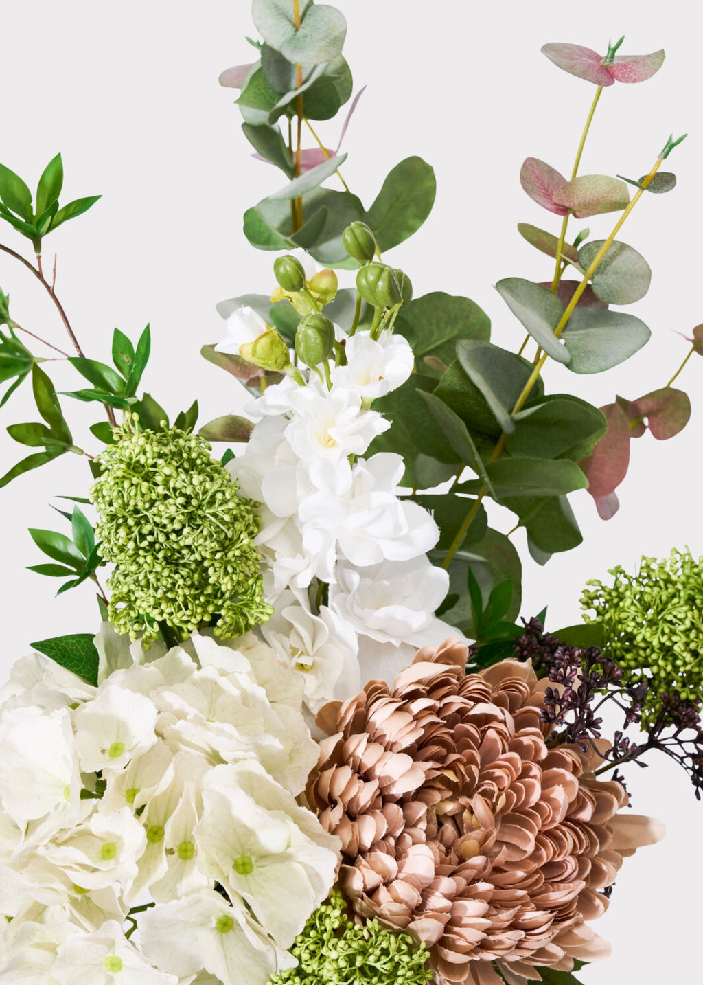 A close-up floral arrangement featuring white flowers, green foliage, and a large dusty rose flower