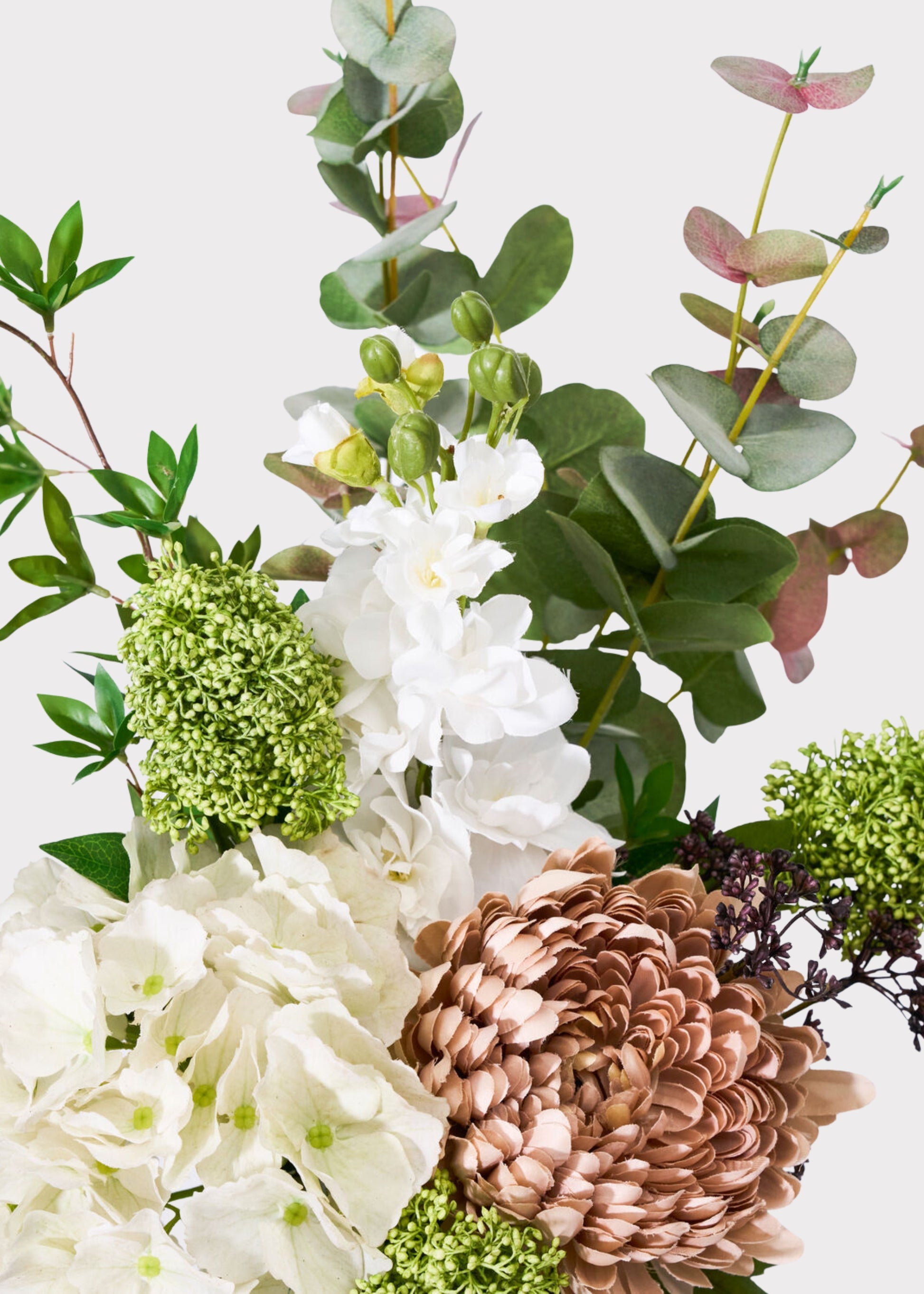 A close-up floral arrangement featuring white flowers, green foliage, and a large dusty rose flower
