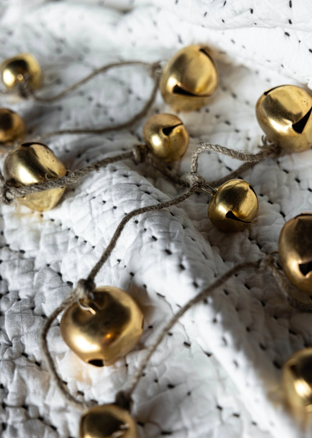A close-up of small metallic gold bells on a string draped over a white textured fabric background.