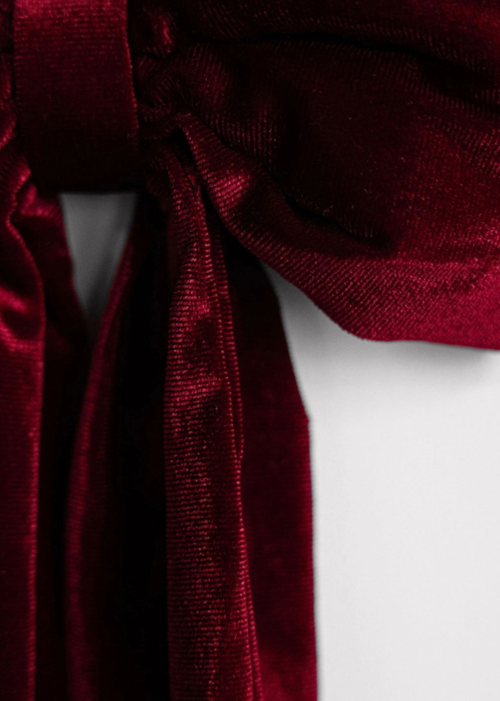 A close-up of a deep burgundy velvet ribbon tied in a bow, showing its rich texture and sheen against a plain white background.