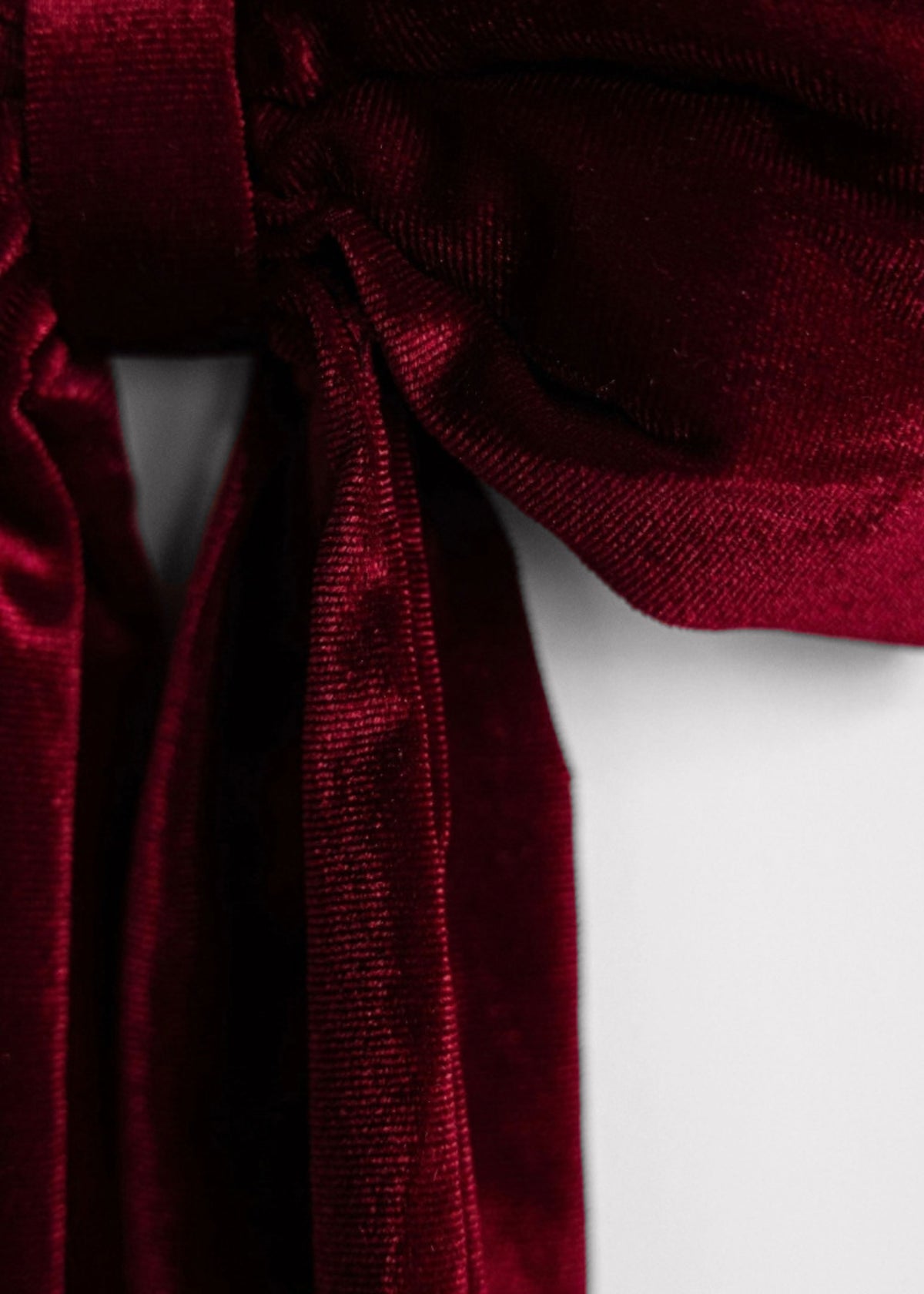 A close-up of a deep burgundy velvet ribbon tied in a bow, showing its rich texture and sheen against a plain white background.