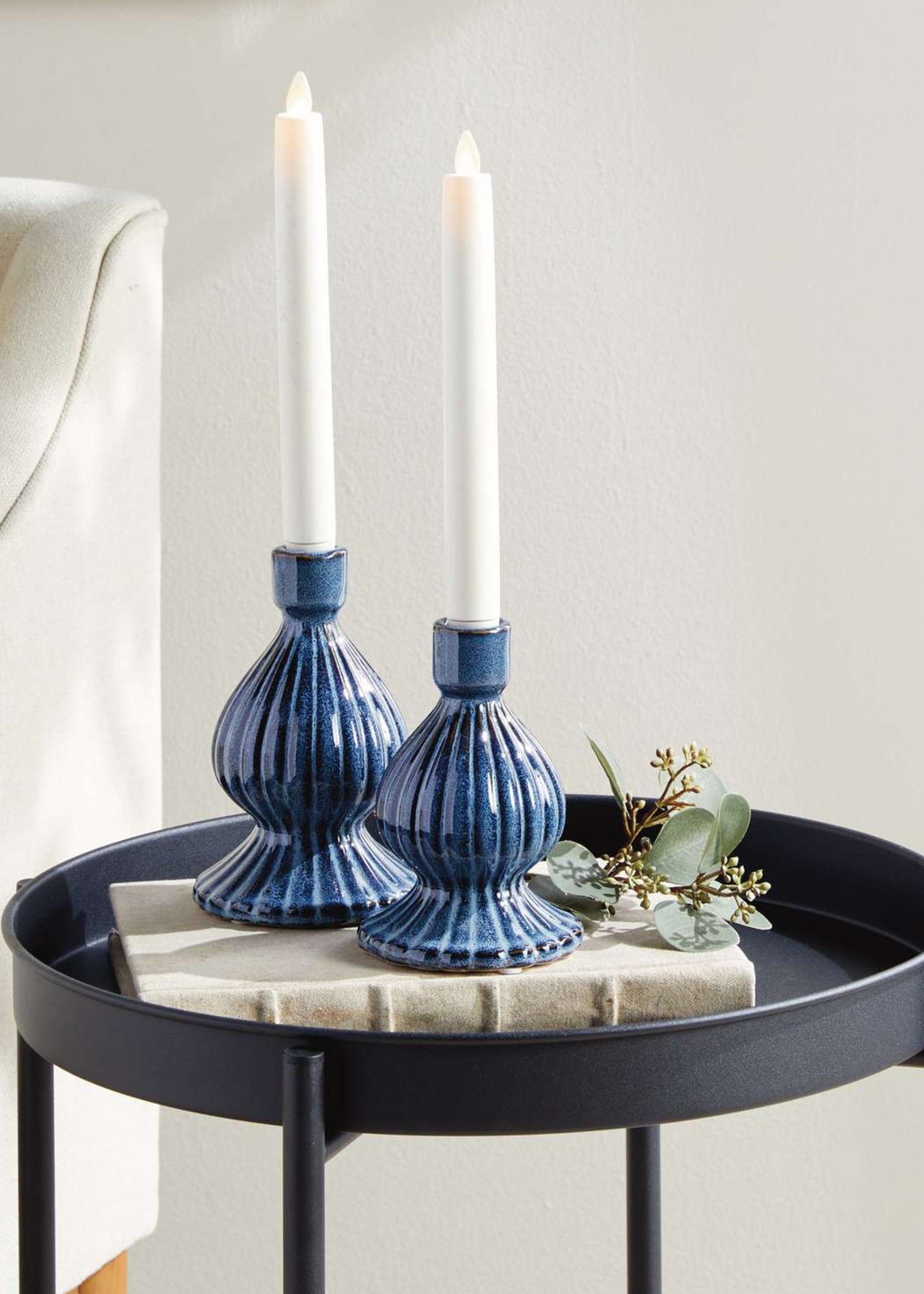 Two blue candle holders with white candles on a round black table.