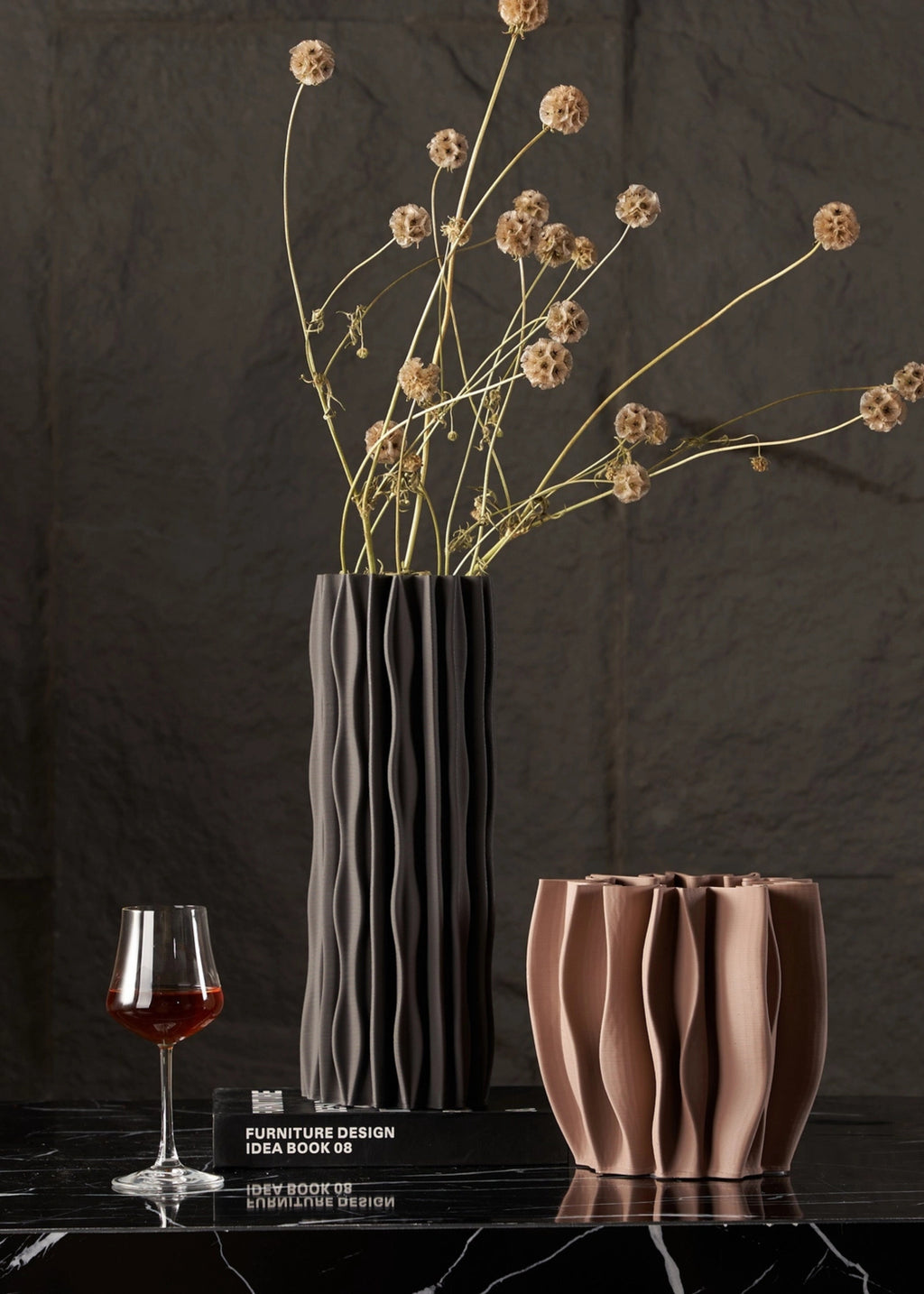 Two vases and a glass of red wine on a dark surface with a dark background