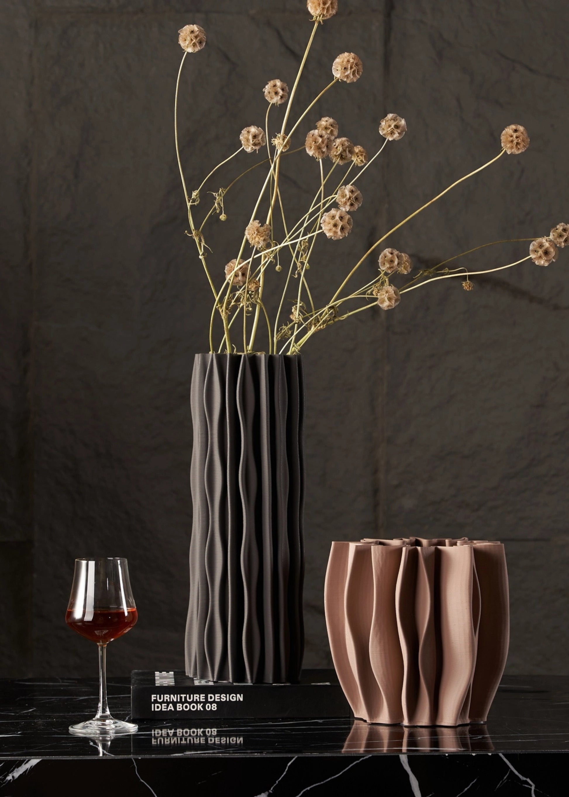 Two vases and a glass of red wine on a dark surface with a dark background