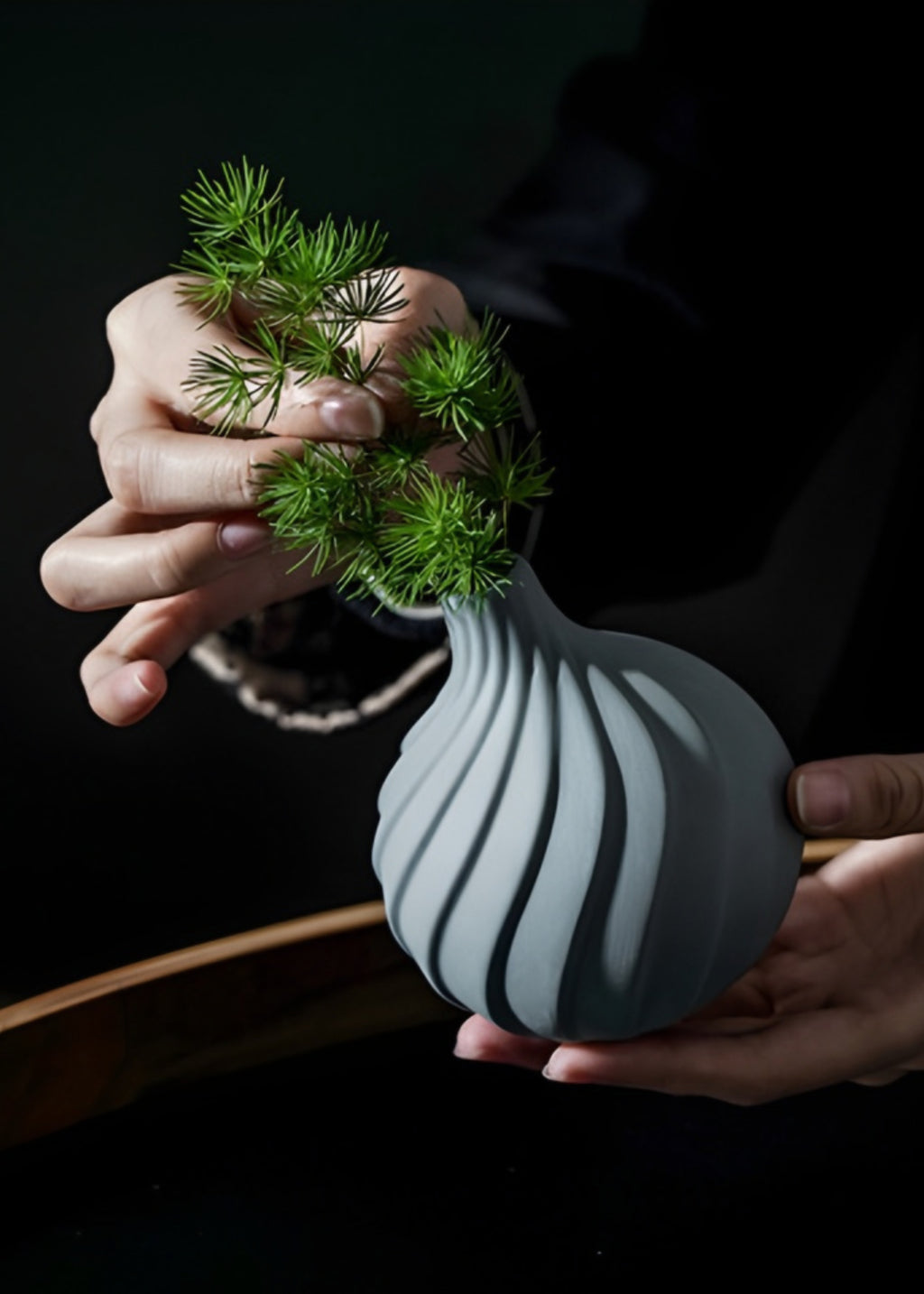 Person holding a ribbed grey ceramic vase 