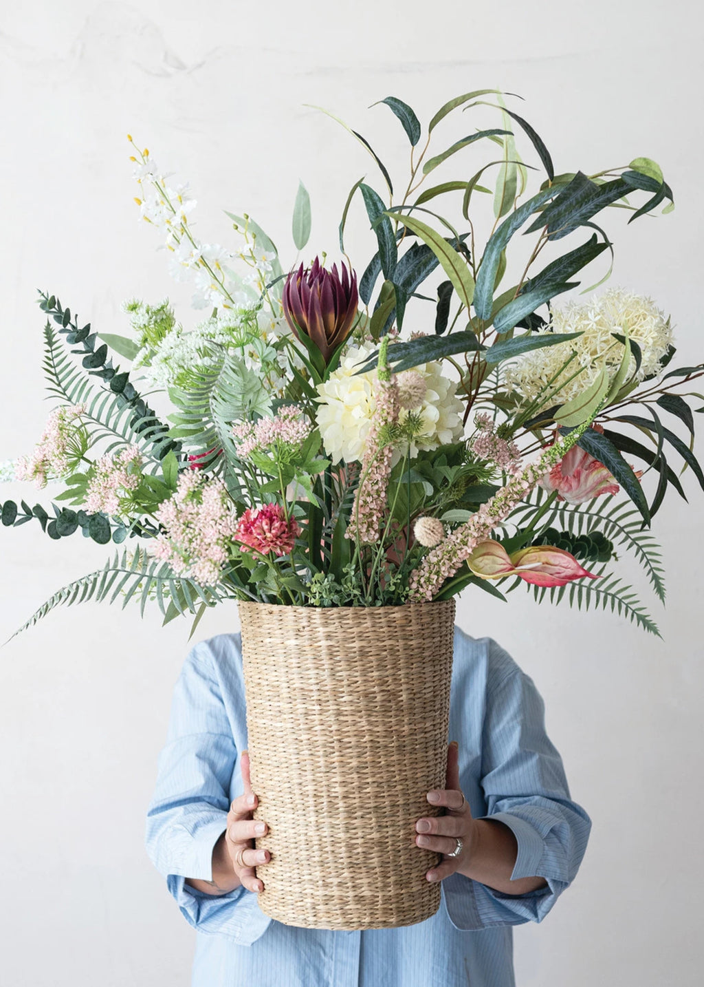 Person holding a large woven basket filled with a colorful arrangement of flowers and plants