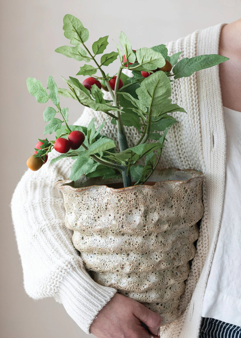 Person holding a textured ceramic planter with an artificial tomato plant