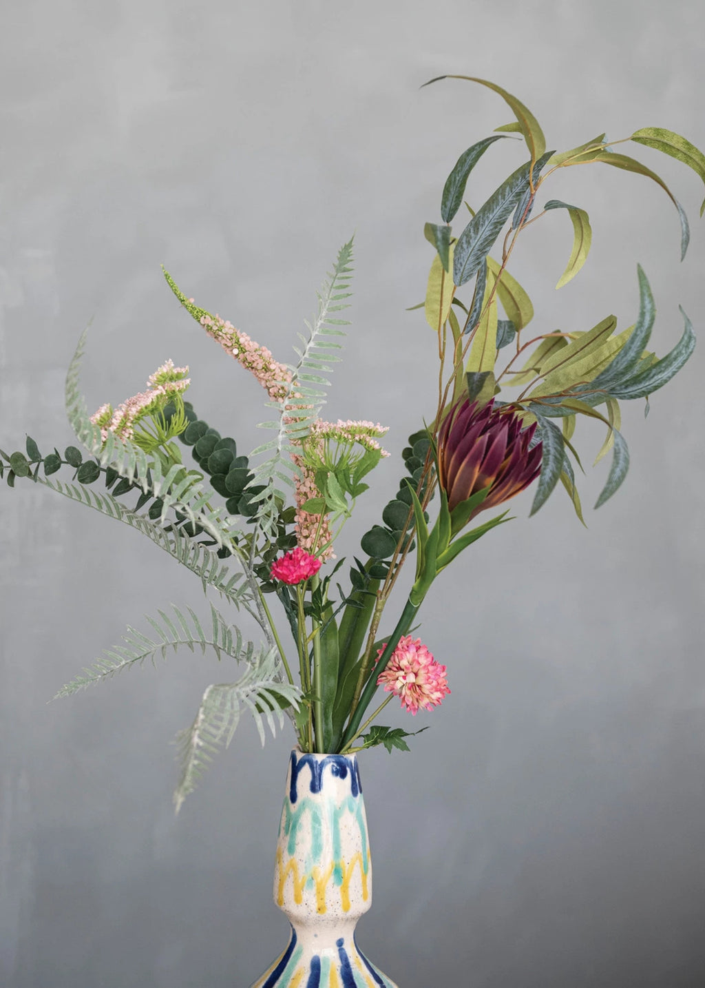 Decorative vase with a colorful pattern containing a bouquet of flowers 