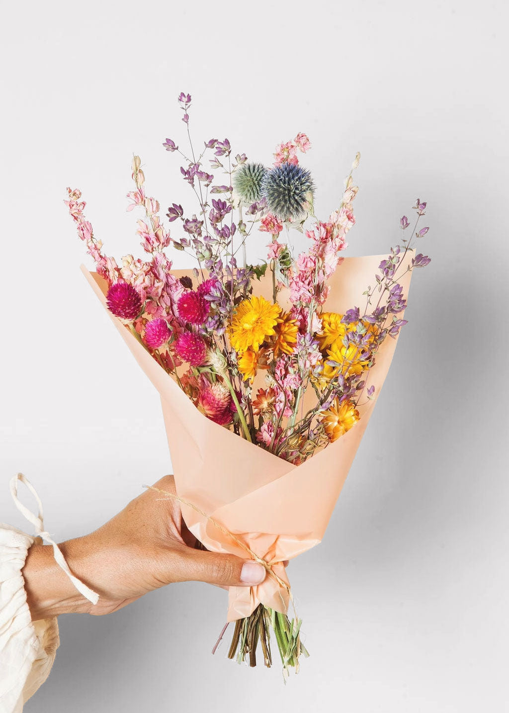 Bouquet of dried flowers wrapped in brown paper held by a person