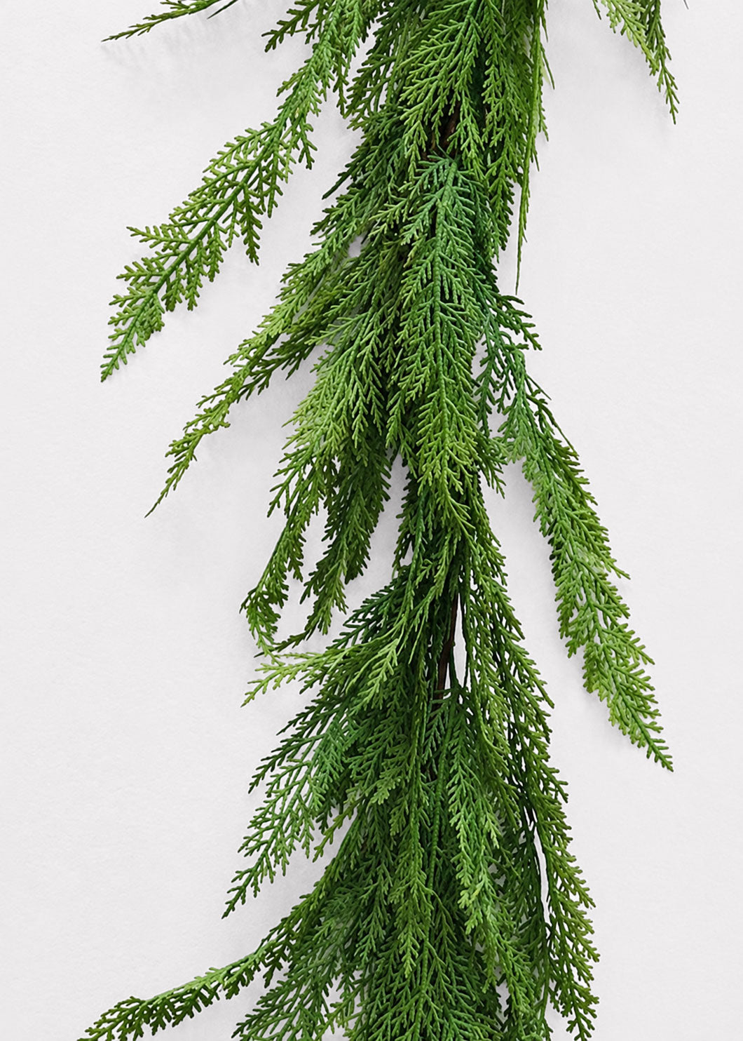Green artificial cedar garland with feathery, needle-like foliage hanging vertically