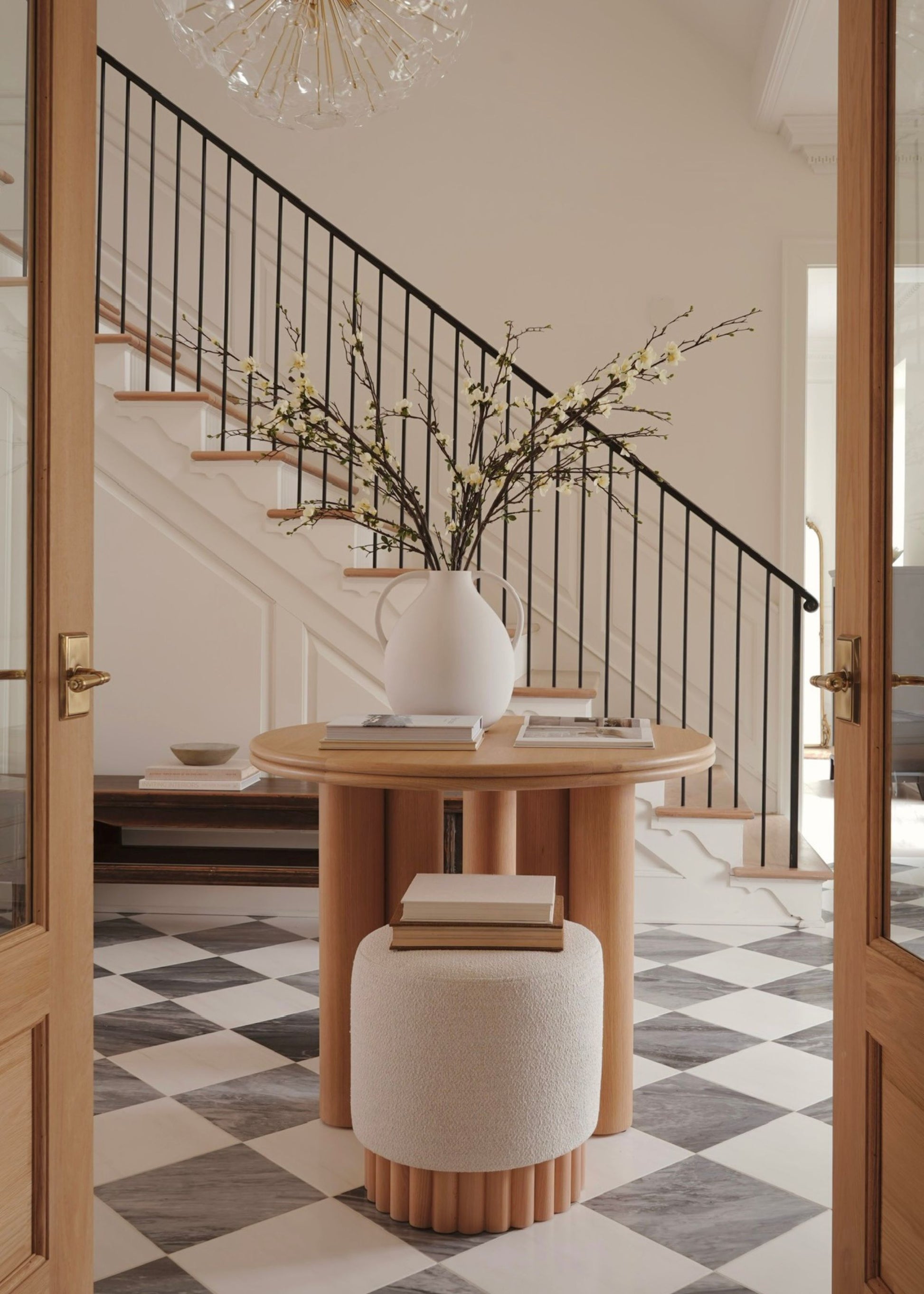 Foyer with a round wooden table, white vase with blossom branches, and checkered floor.
