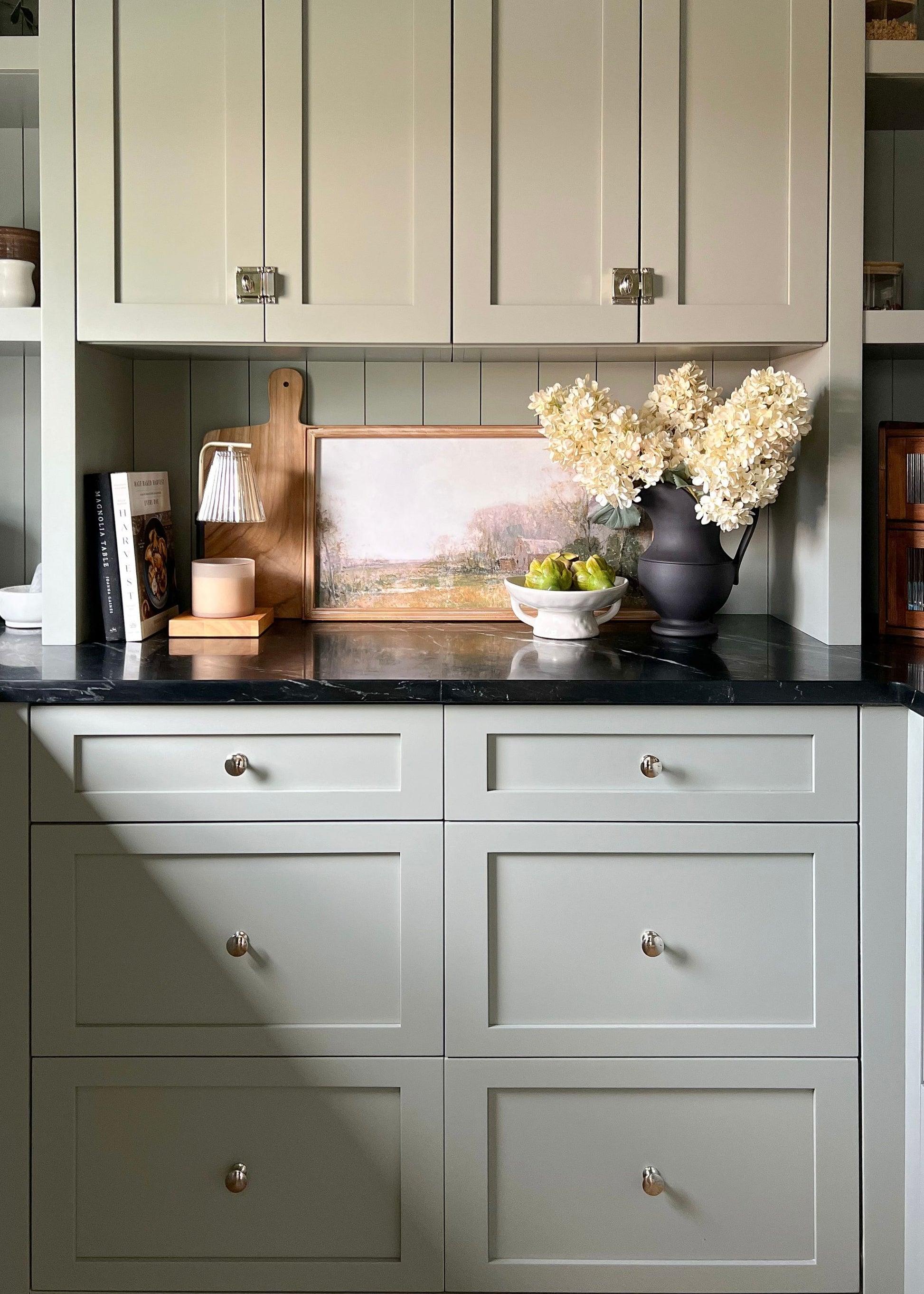 Large dried-look faux hydrangeas styled in a black pitcher vase on a pantry shelf