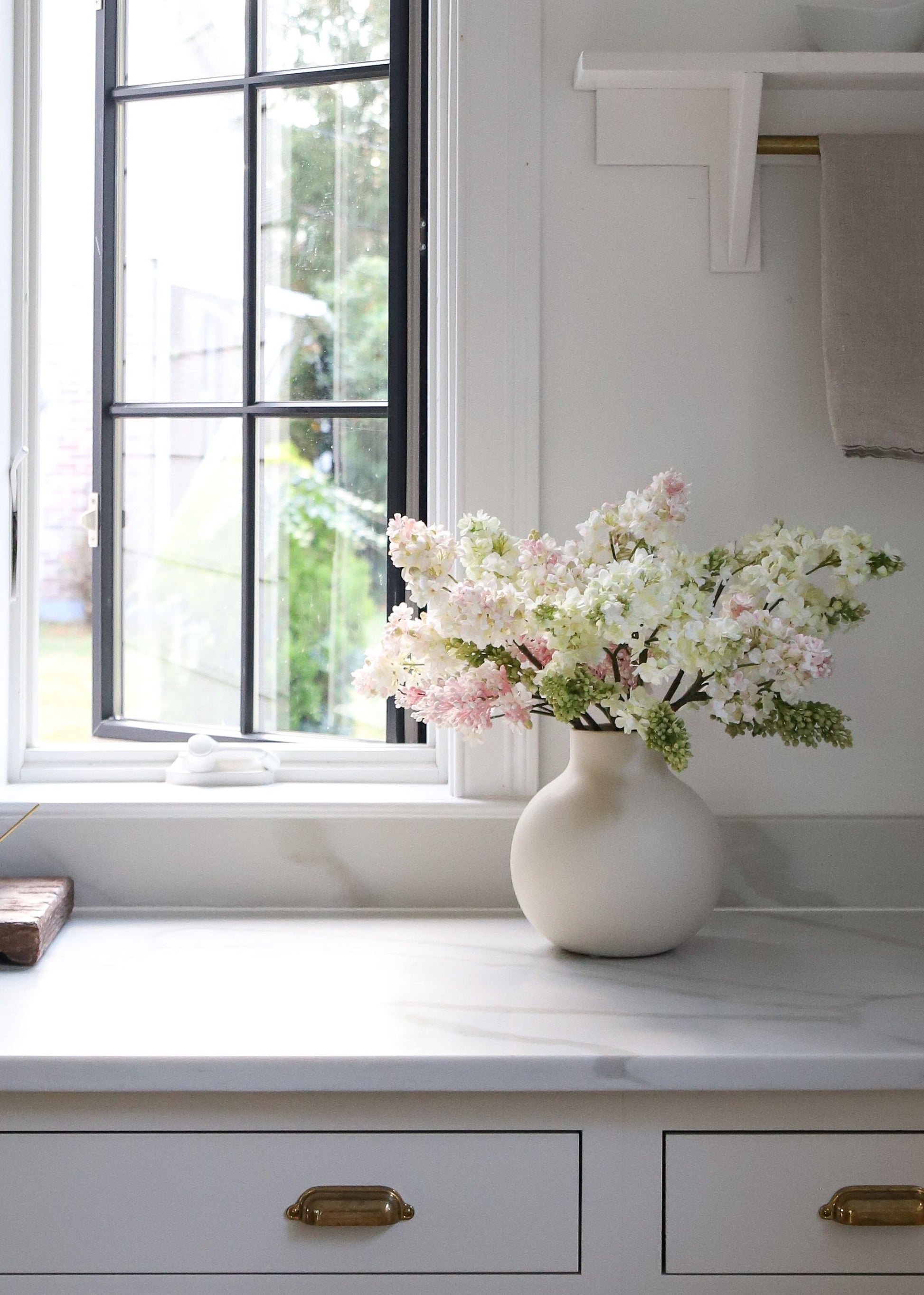 White vase with pink and cream lilac flowers on a kitchen counter