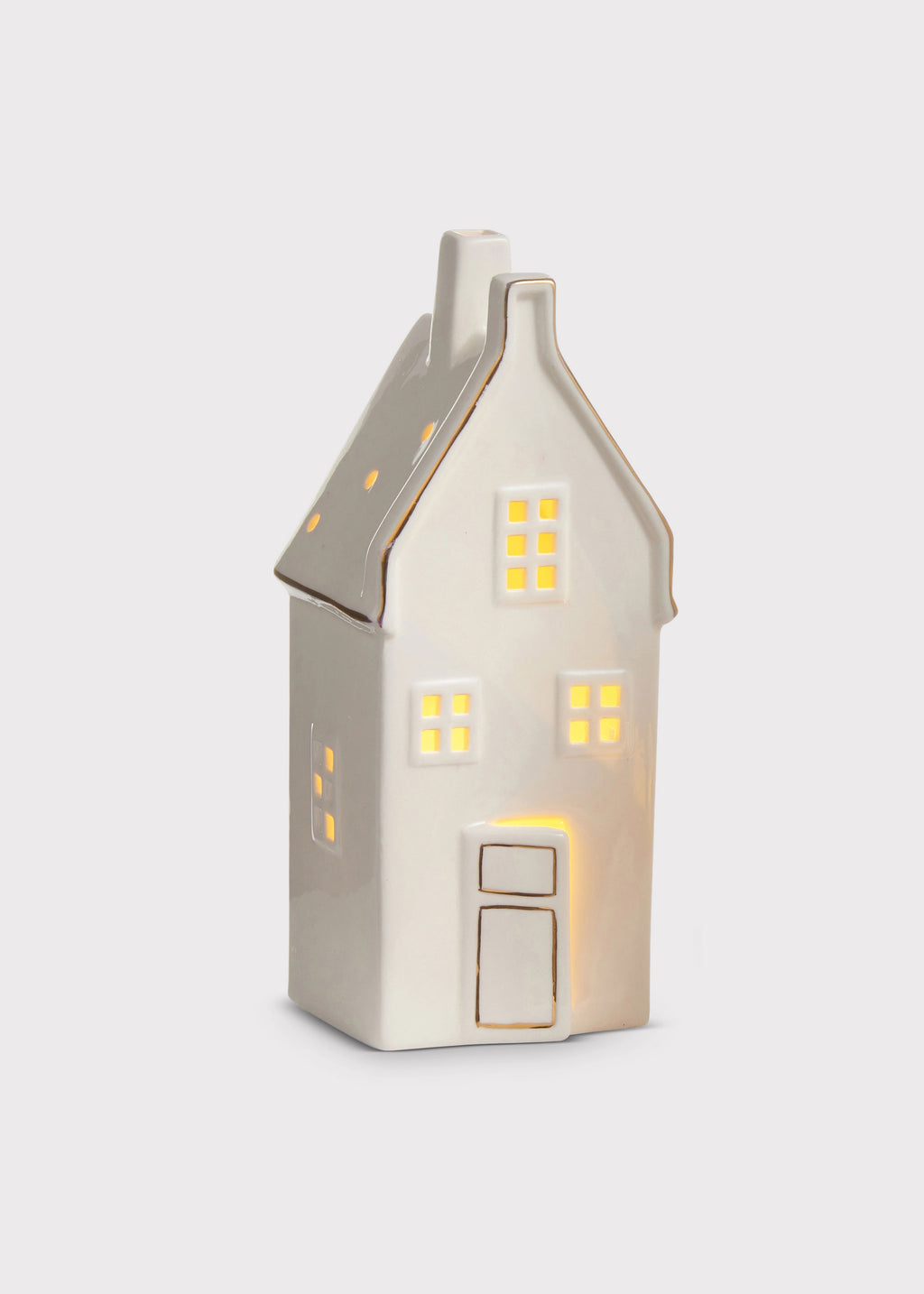 A small ceramic house-shaped light with a warm white body, gold trim, and glowing yellow window lights, shown on a light gray background.