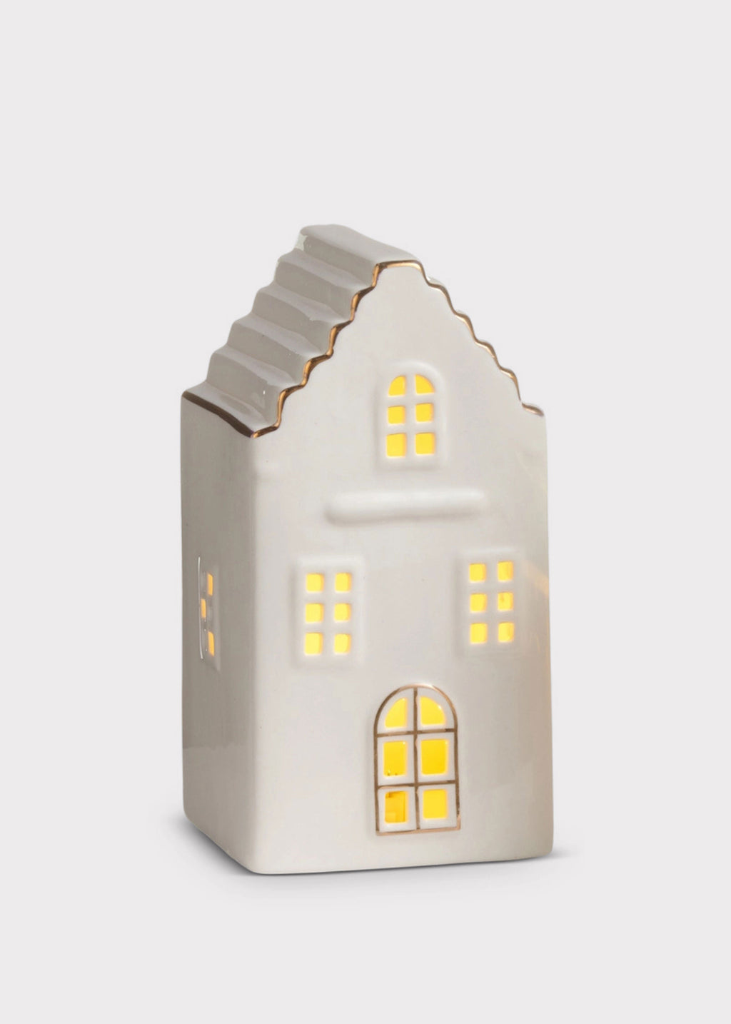 A small ceramic house-shaped light with a warm white body, gold trim, and glowing yellow window lights, shown on a light gray background.