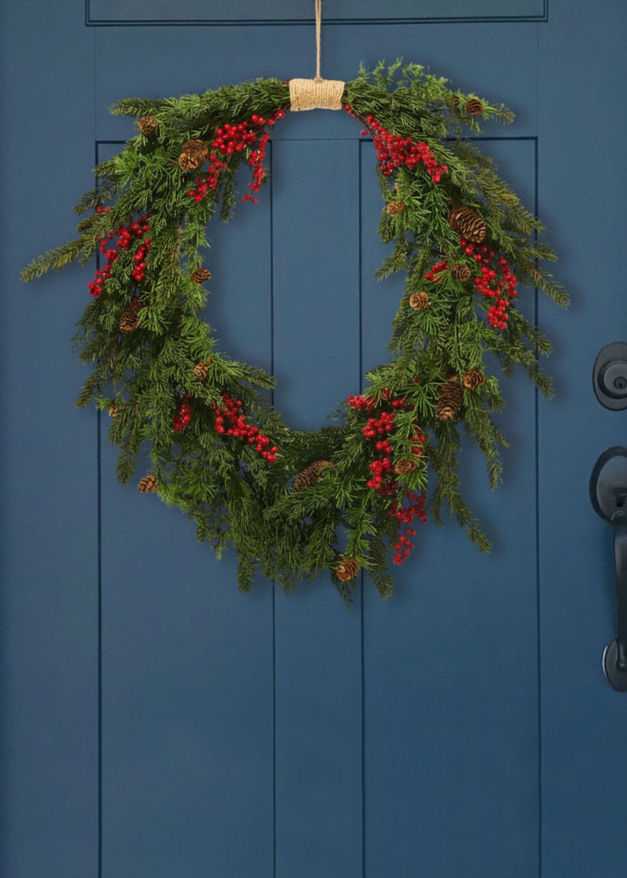 fake cedar wreath with pine cones and red berries on a blue door
