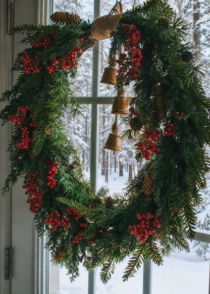 Decorative Christmas wreath with red berries and pine cones hanging on a door 