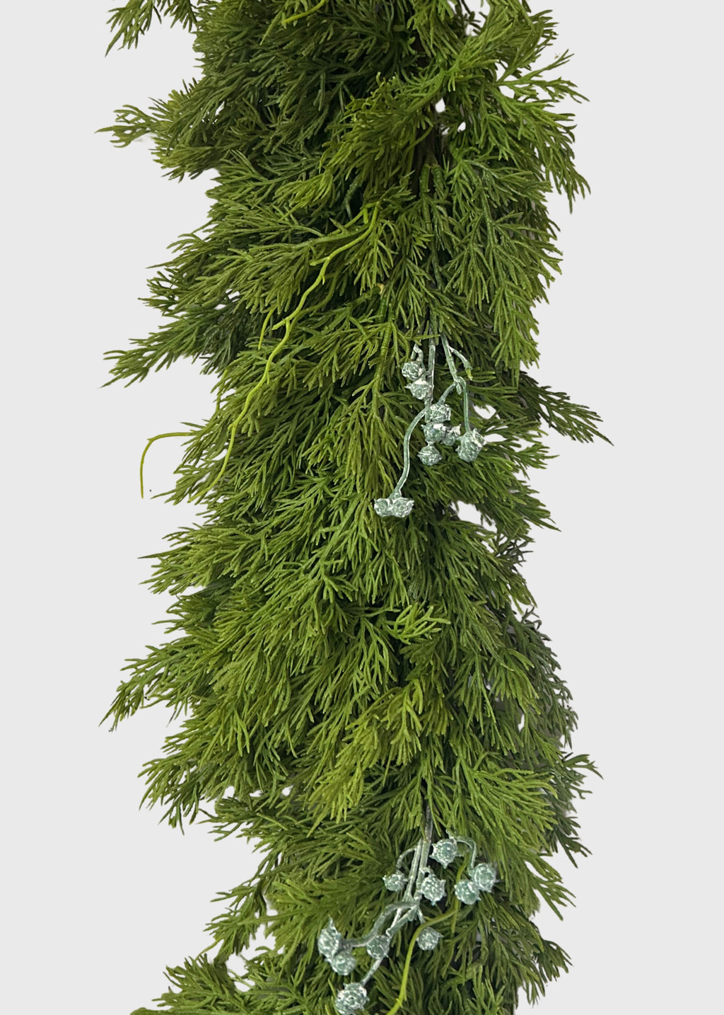 A close-up of a green artificial juniper garland with dense, needle-like foliage and small pale green blue berry-like accents