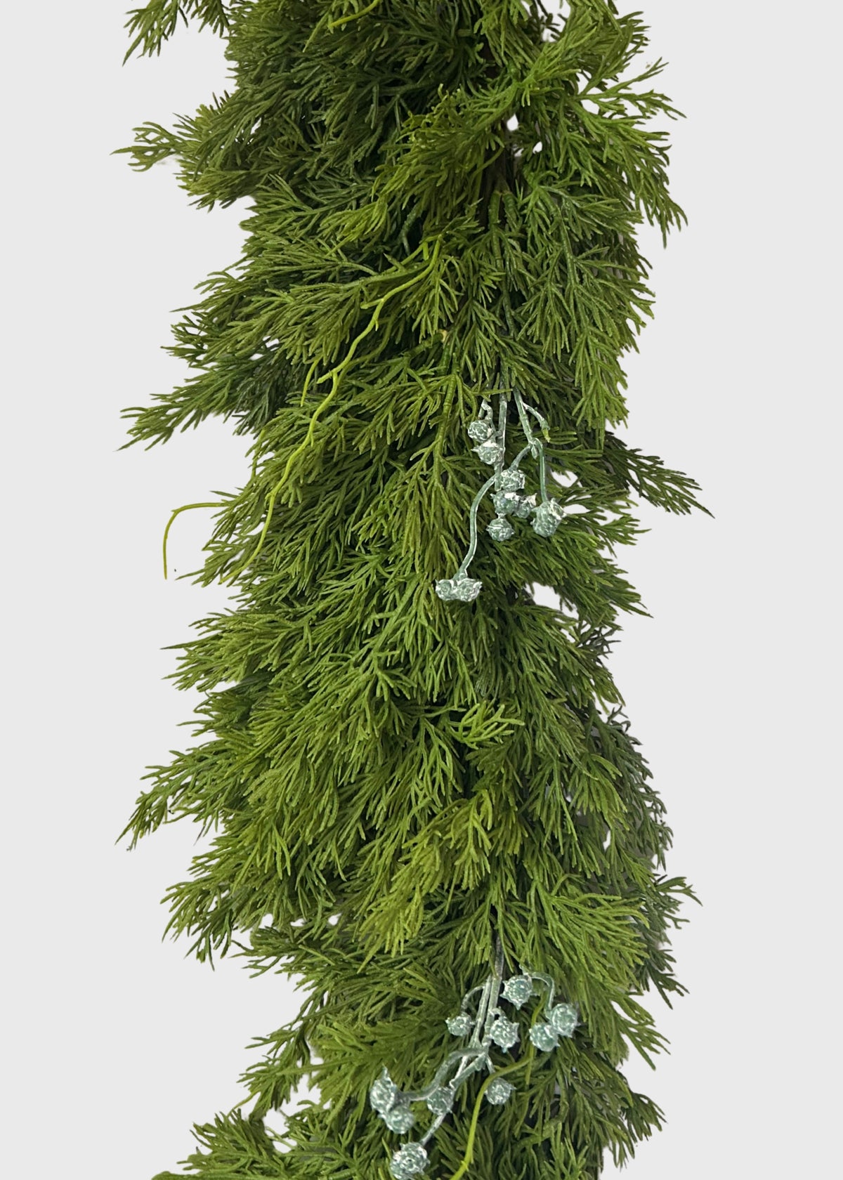 A close-up of a green artificial juniper garland with dense, needle-like foliage and small pale green blue berry-like accents