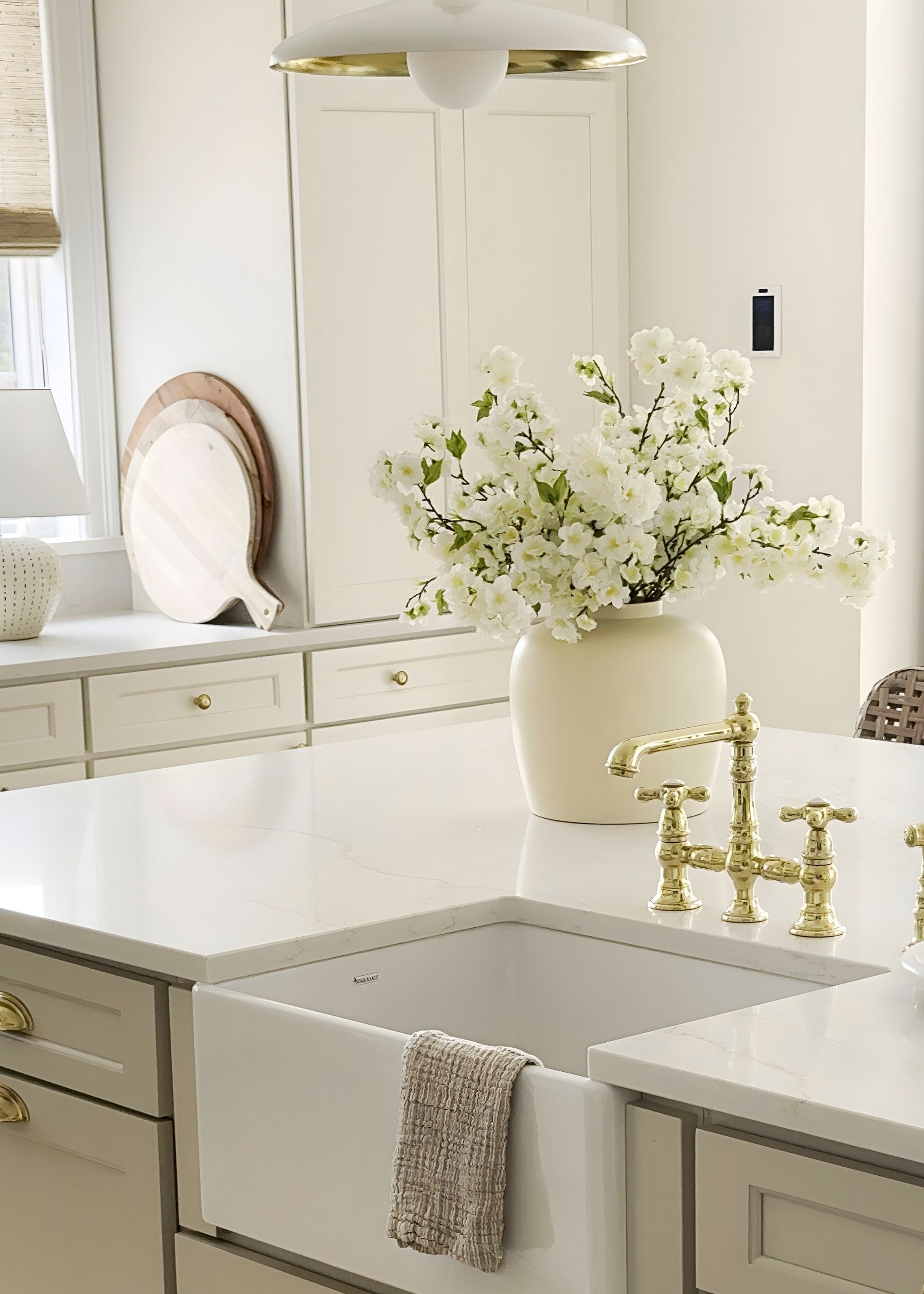 Kitchen with white cabinets, gold fixtures, and a vase of white cherry blossom flowers on the counter.