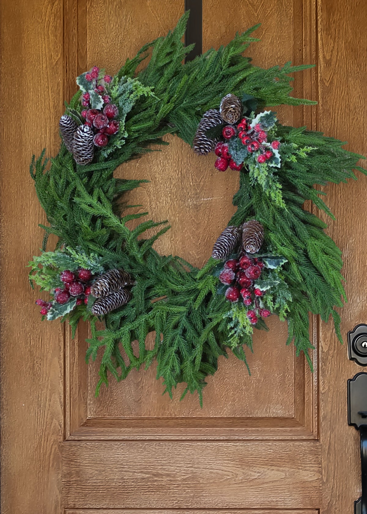 Fake Cedar and Pine Cone Pick with Red Beaded Berries Decorating a Norfolk Pine Wreath on a Wood Door